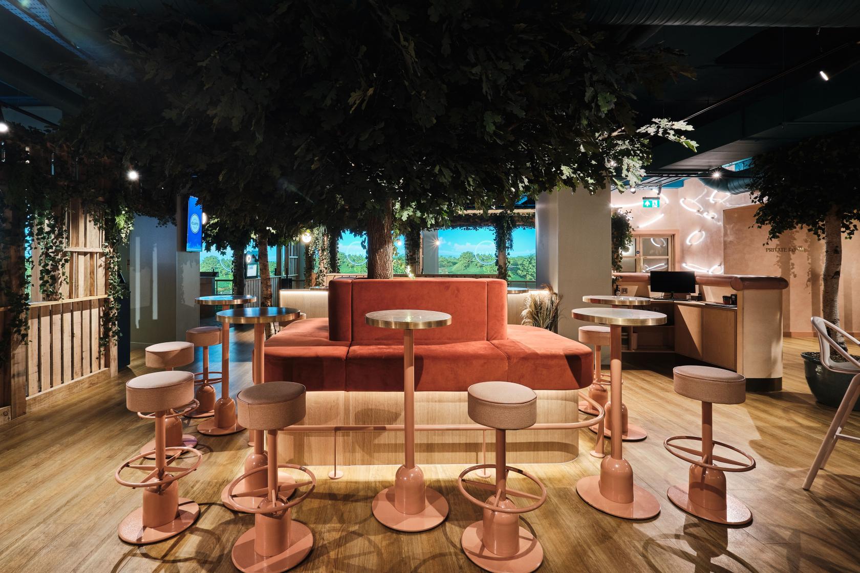 An event space with pink bar stools, round tables, and greenery hanging from the ceiling at Clays City.