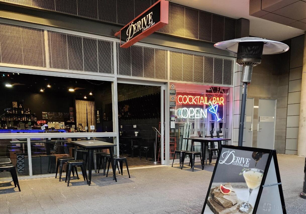 A bar with outdoor seating, neon cocktail bar sign, and an overhead heater at Derive Cocktail Bar.
