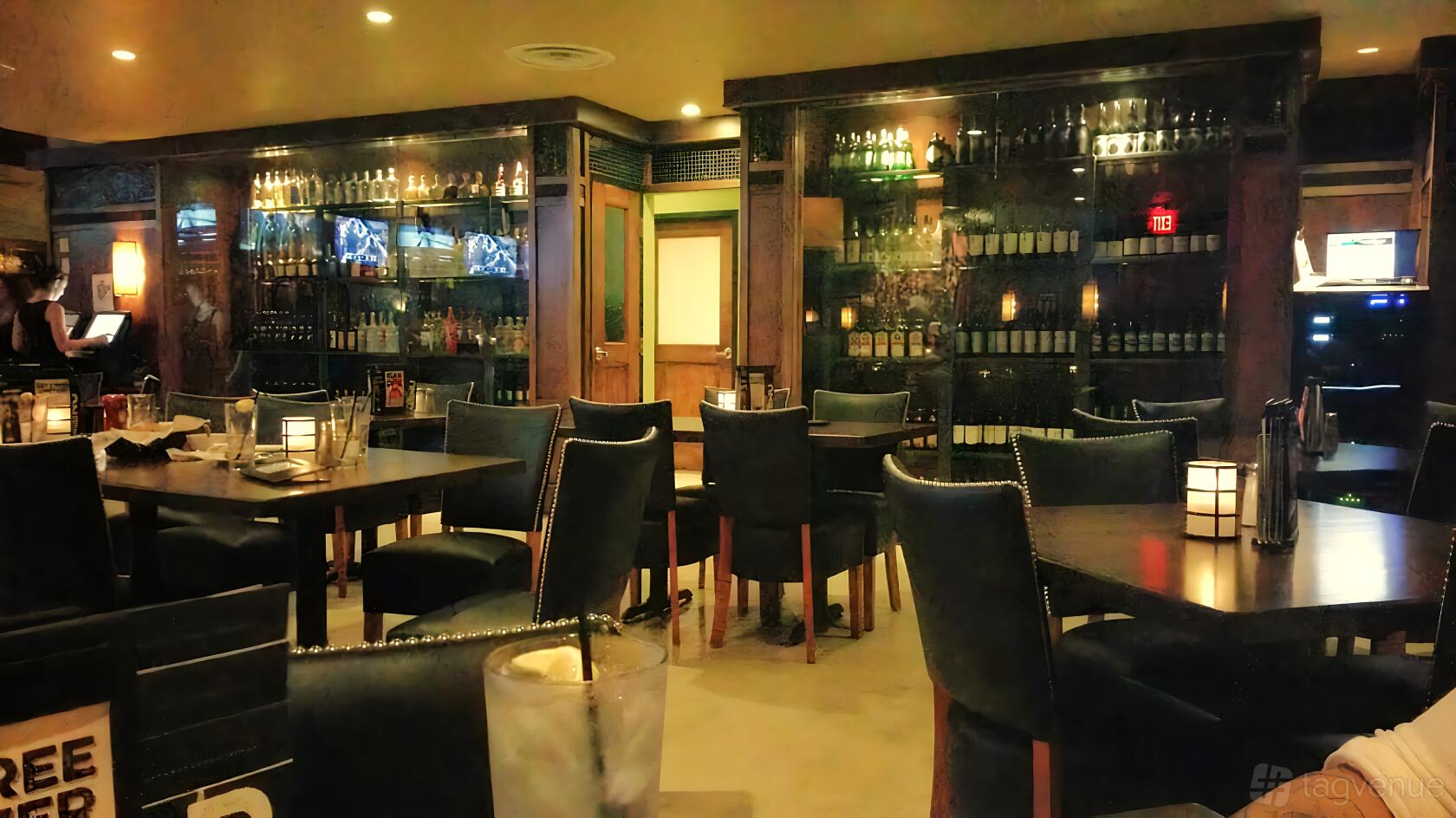 A bar with dark wood shelves lined with bottles, black upholstered chairs, and candlelit tables at Bar Louie - Coconut Creek.