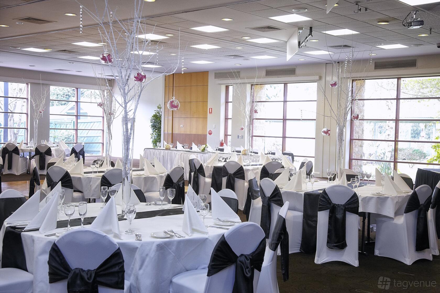 An event space in a pub with round tables dressed in white linens and black chair sashes at York On Lilydale.