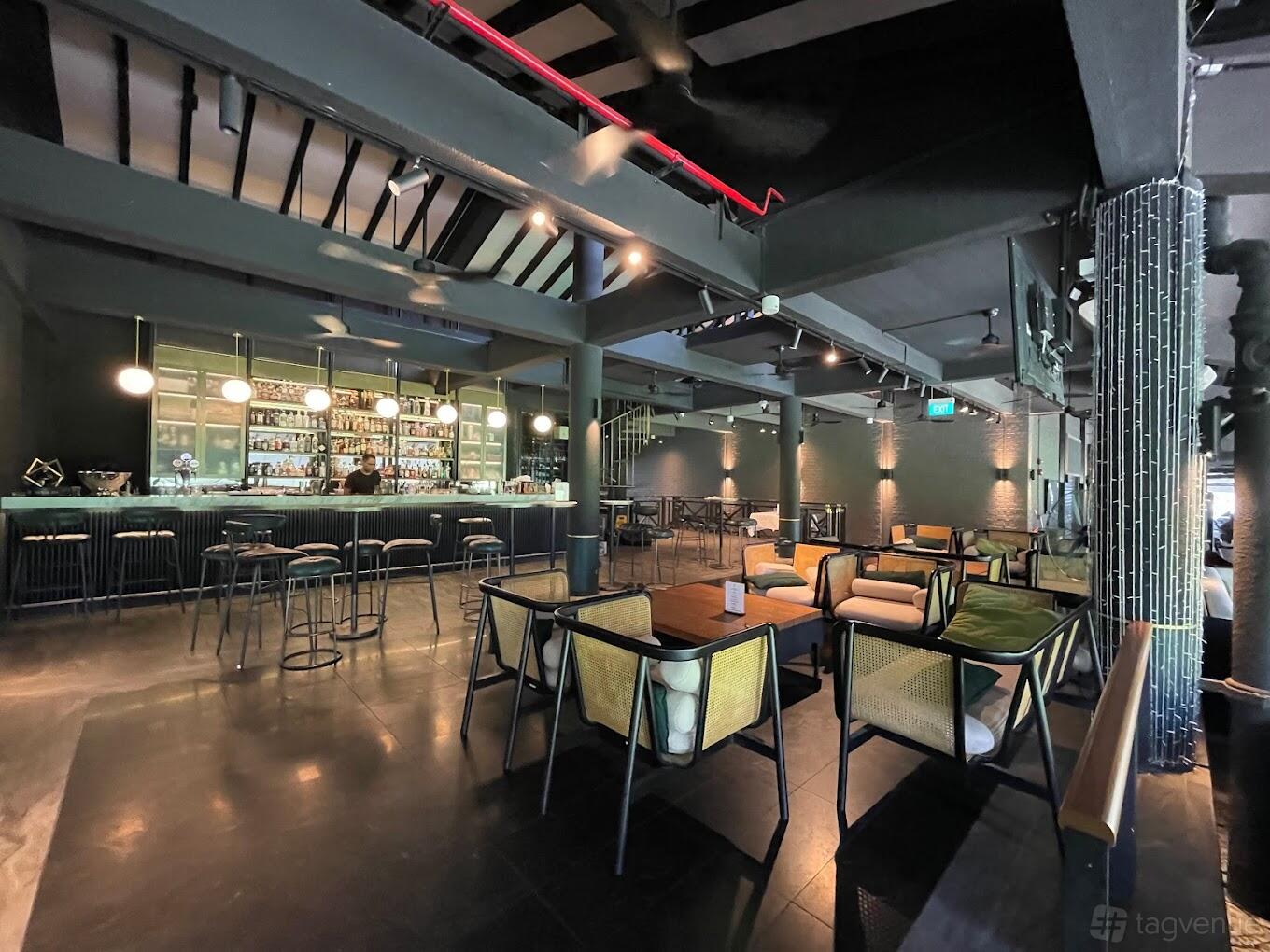 A bar in a restaurant with a long backlit counter, rattan chairs, and modern pendant lights at Coriander Leaf @ Polo Club.