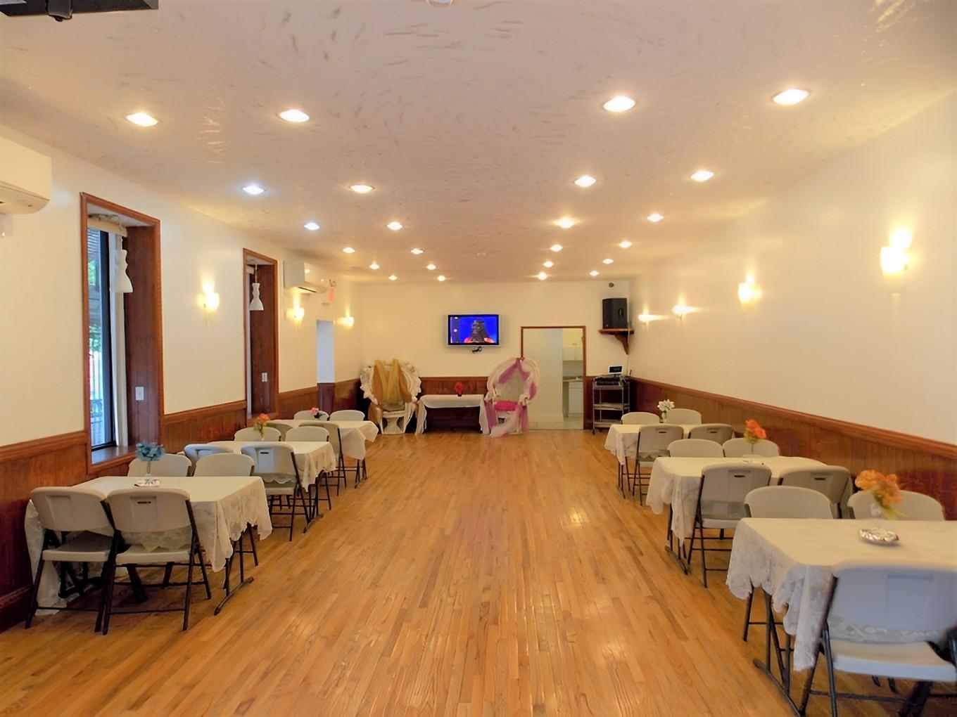 A hall with wood floors, white walls, ceiling lights, and rectangular tables covered with white cloths at Cacin Hall.