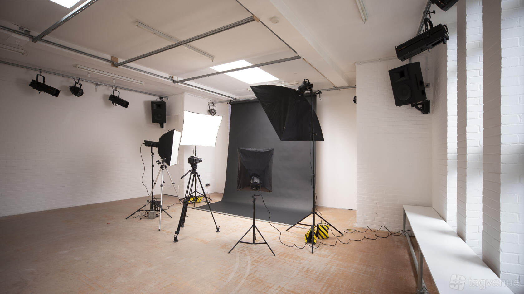 A photo studio with lighting equipment, tripods, and a gray backdrop near large windows at Kunstraum.
