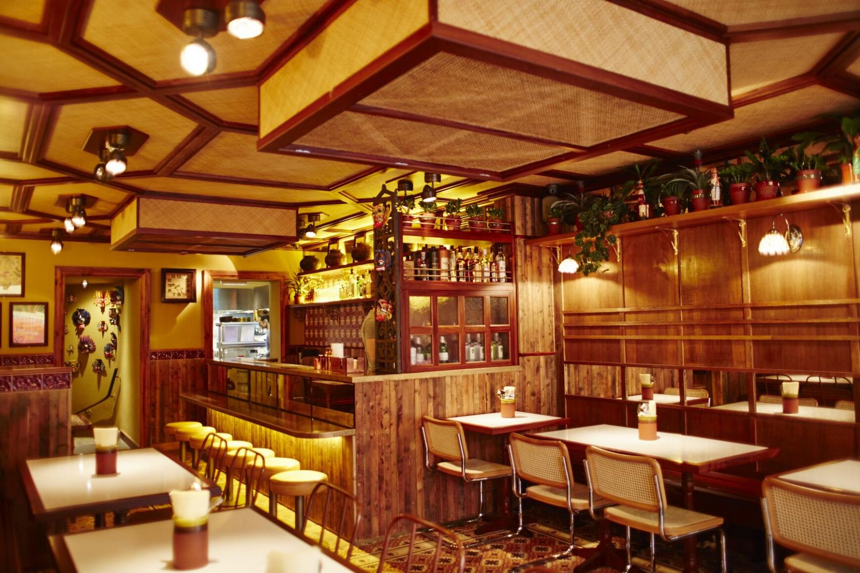 A restaurant dining area with wooden paneling, potted plants, and rattan ceiling accents at Hoppers Soho.