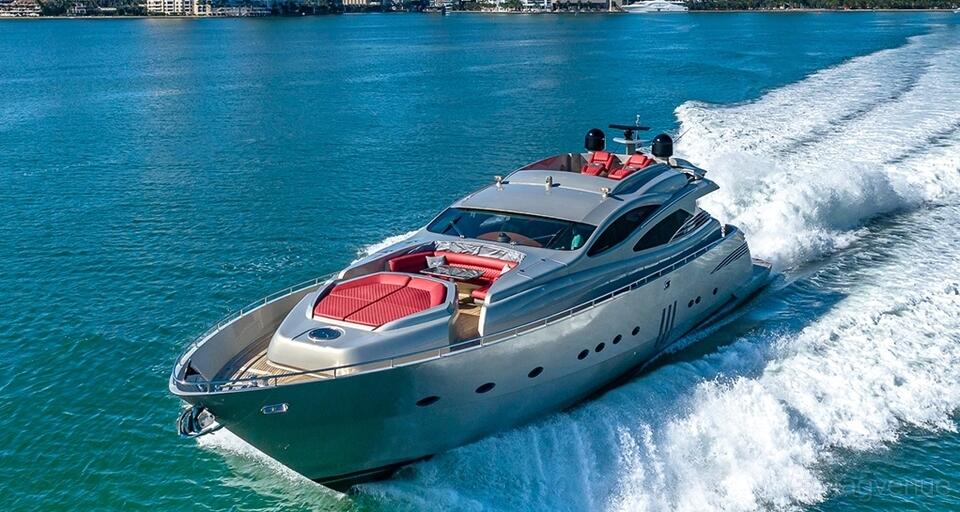 A luxury yacht with a sleek silver exterior and red lounge seating cruising on open water at UNIQ YACHT CHARTERS