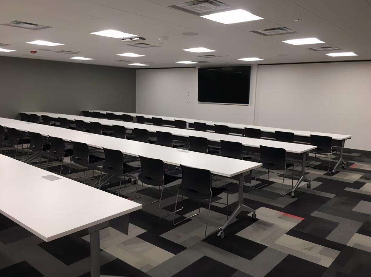 A training room with rows of white tables, black chairs, and a large wall-mounted screen at YourOffice – Denver.