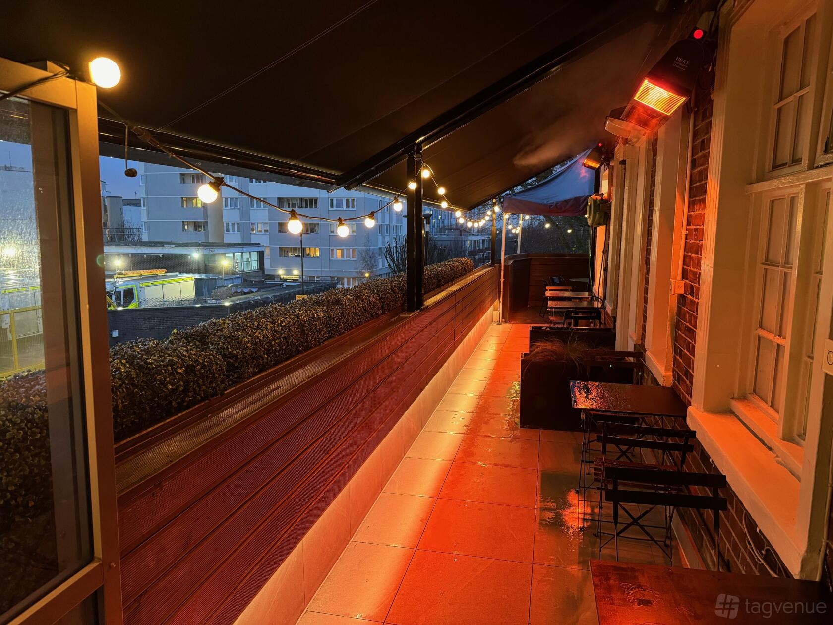A covered terrace bar with string lights, small tables, and outdoor heaters at The Chapel Bar.