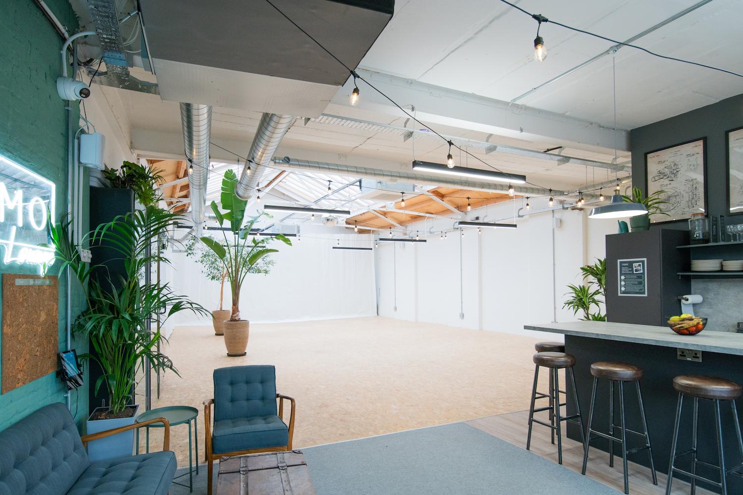 A coworking space with skylights, exposed ducts, potted plants, and a lounge area at FOMO House Shoreditch.