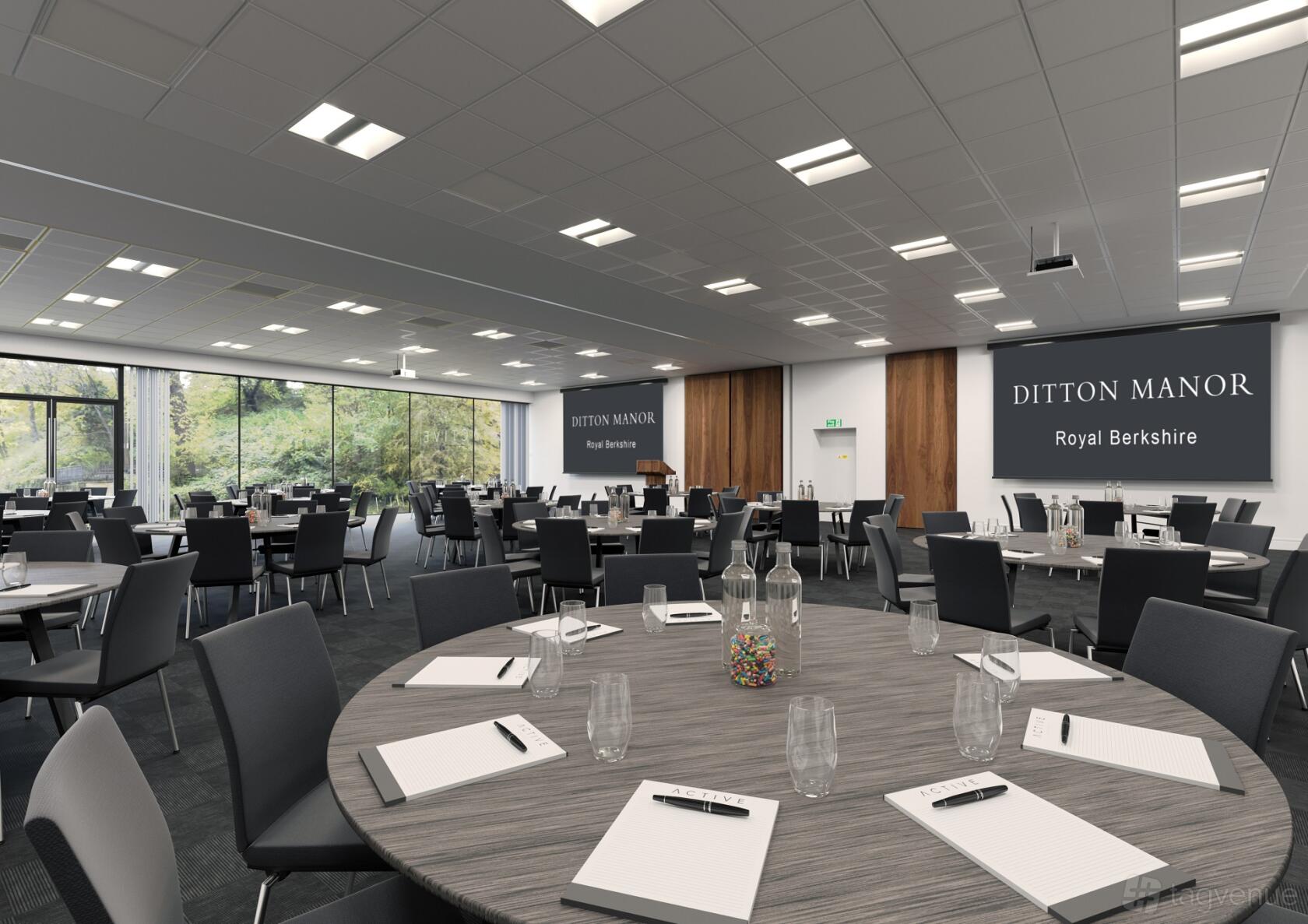 A meeting room with round tables, notepads, black chairs, floor-to-ceiling windows, and projection screens at Southgate Conference Centre.