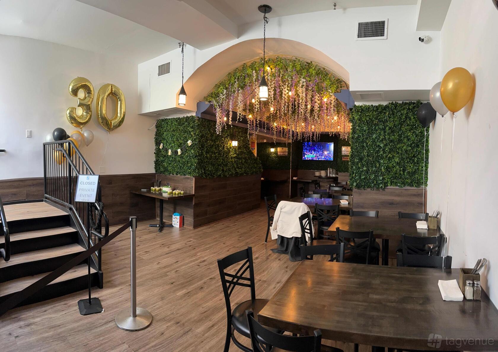 A function room with greenery walls, hanging floral decor, and wooden floors at Alexandria Bier Garden.