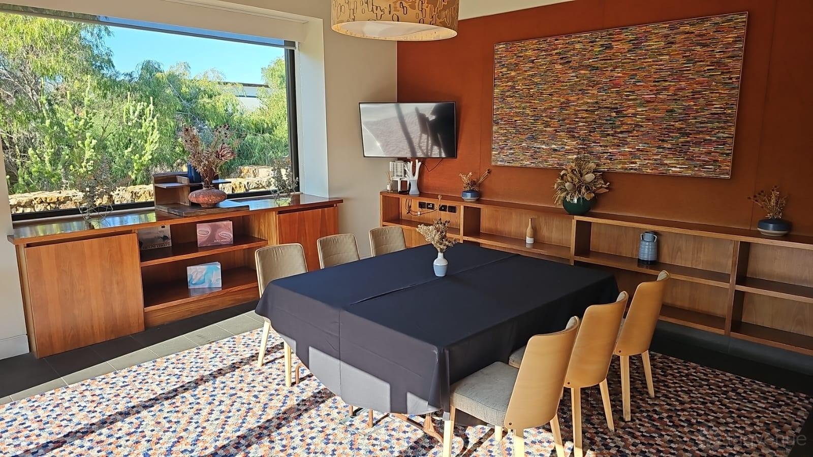A hotel meeting room with a rectangular table, light wood chairs, wall-mounted TV, and large window at Pullman Bunker Bay.