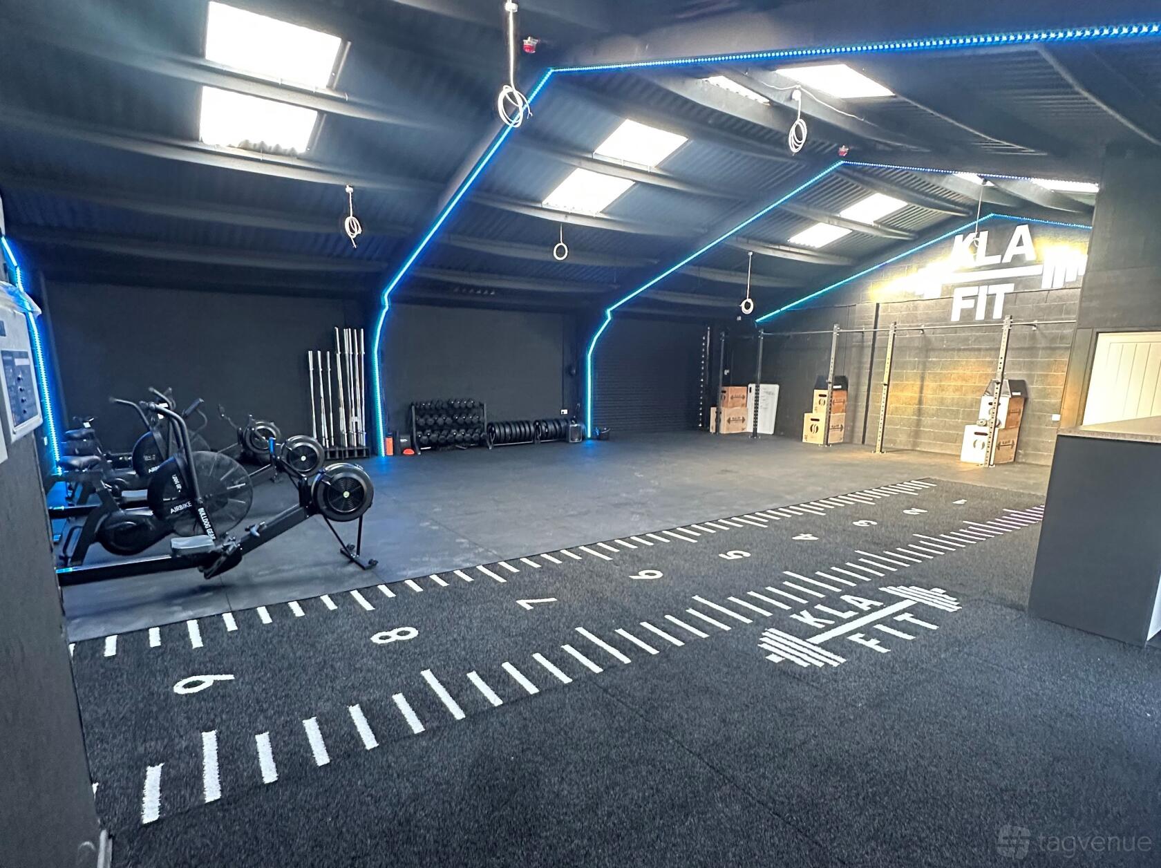 A fitness studio with turf flooring, cardio machines, free weights, and LED ceiling lights at KLA FIT.