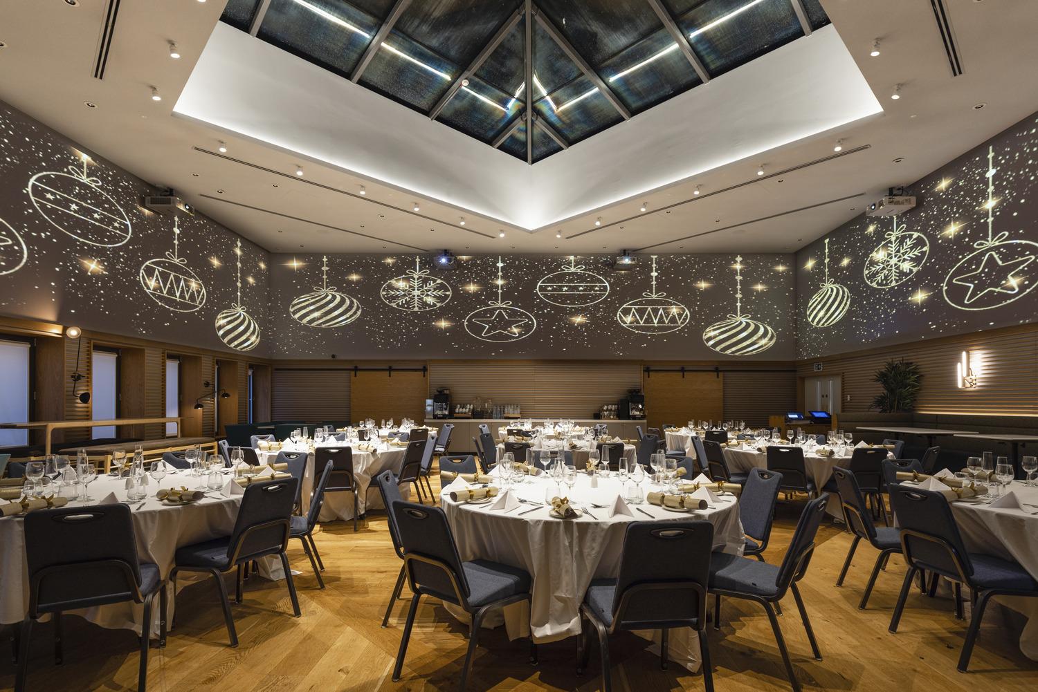An auditorium with a glass ceiling, patterned wall projections, and round tables set for dining at YOTEL Edinburgh.