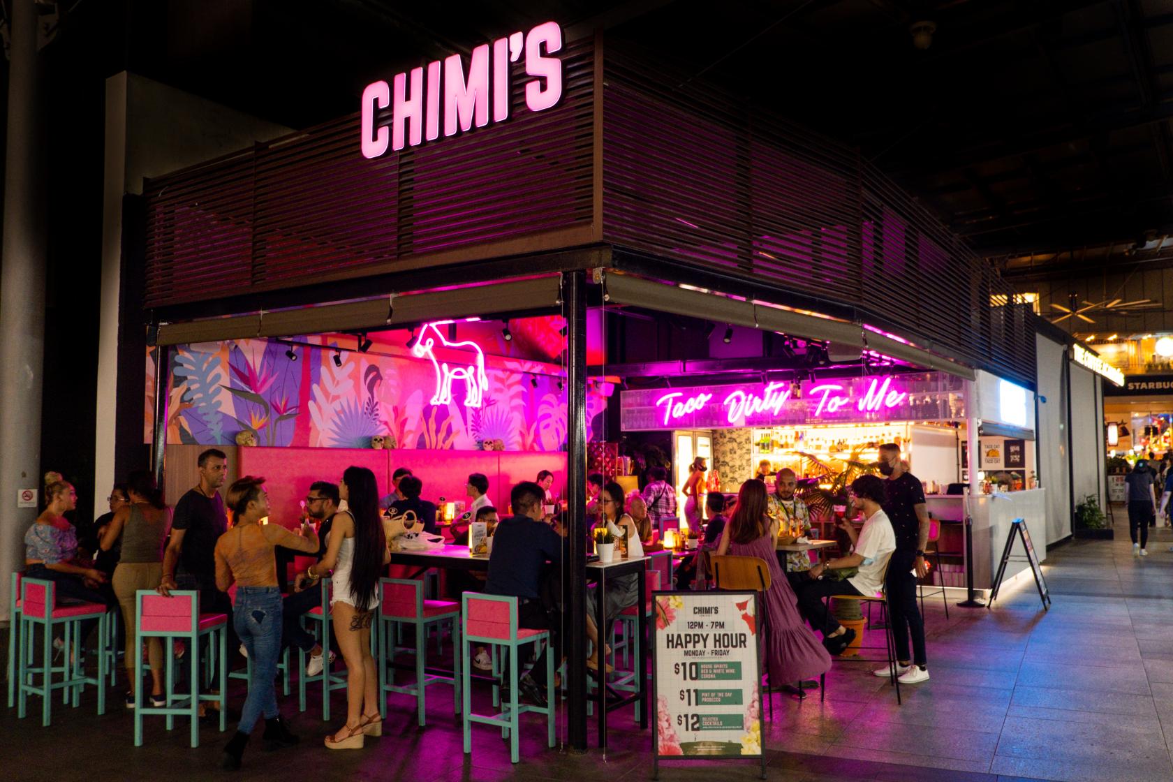 An open-air restaurant with neon pink lighting, high tables, and tropical murals at Chimi's Somerset.
