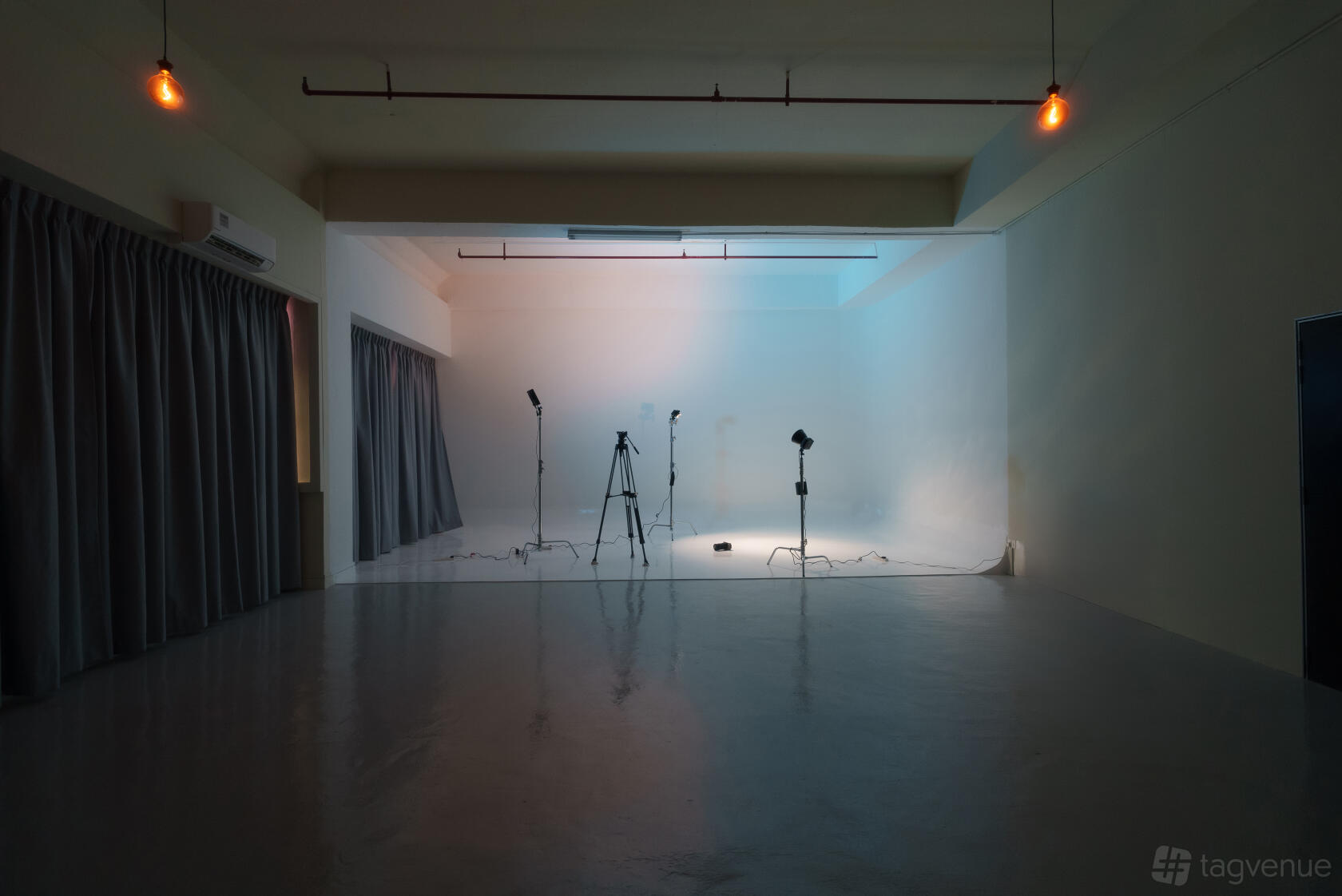 A photo studio with a seamless white backdrop, three tripods, and overhead industrial lighting at Think Beyond Hues | TBH Media.