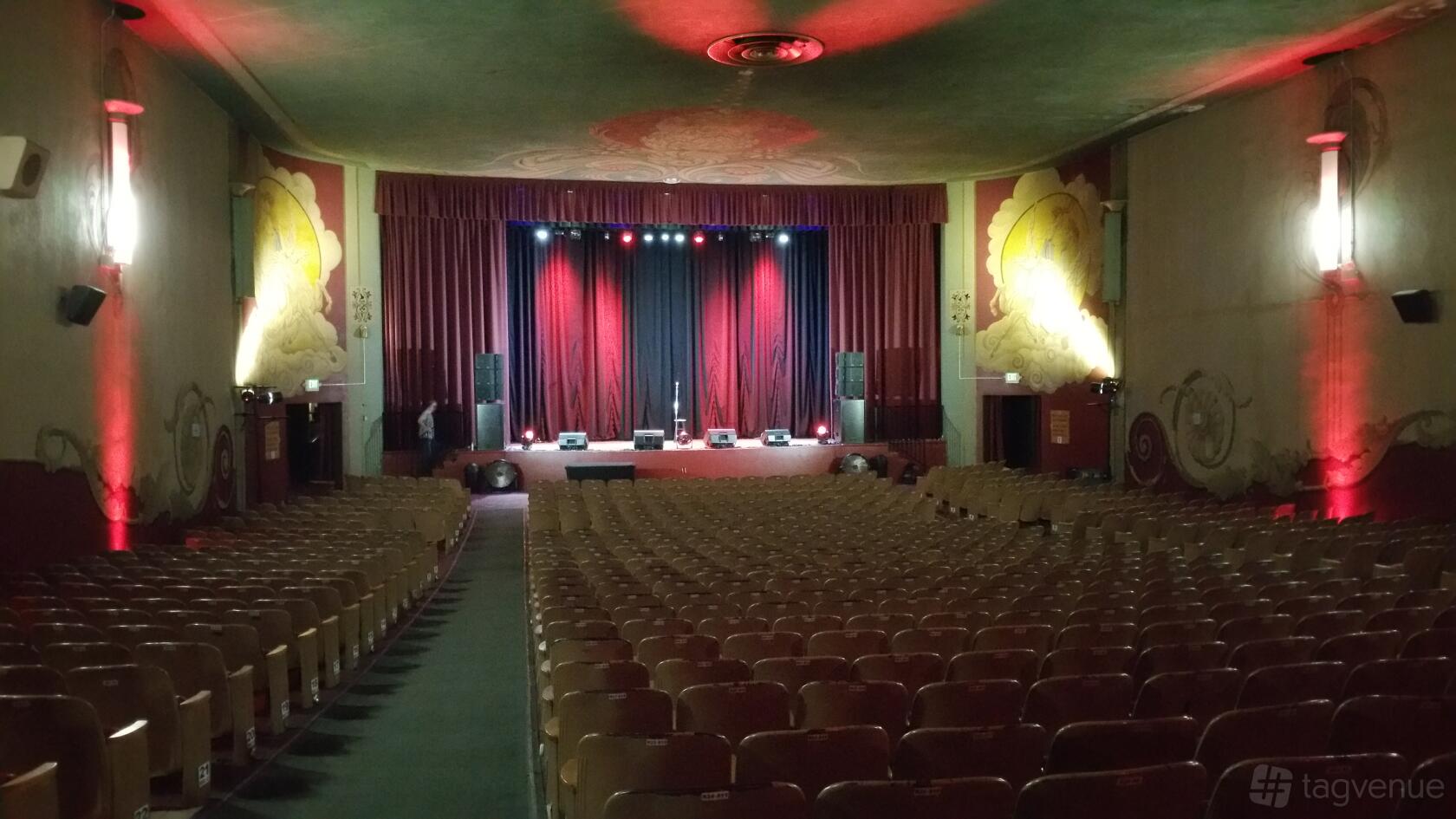 A theatre with a large stage, red curtains, and rows of wooden seats at Historic BAL Theatre.