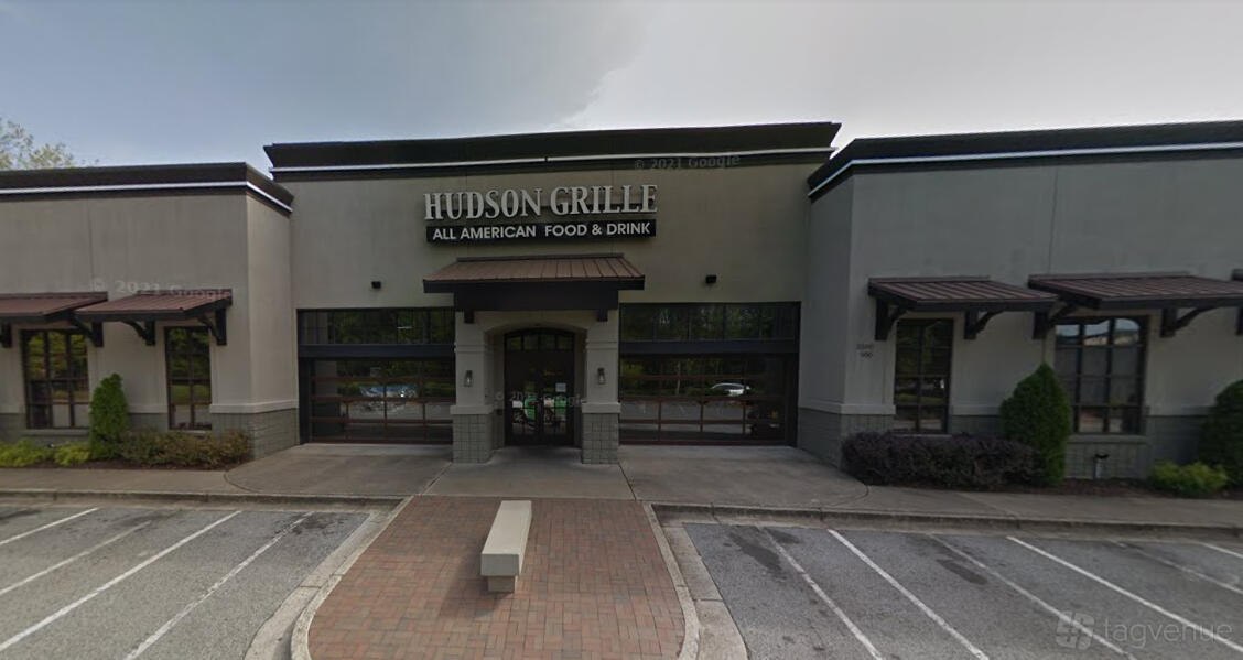 A pub with a wide entrance, large front windows, and awnings over the doors at Hudson Grille - Kennesaw.
