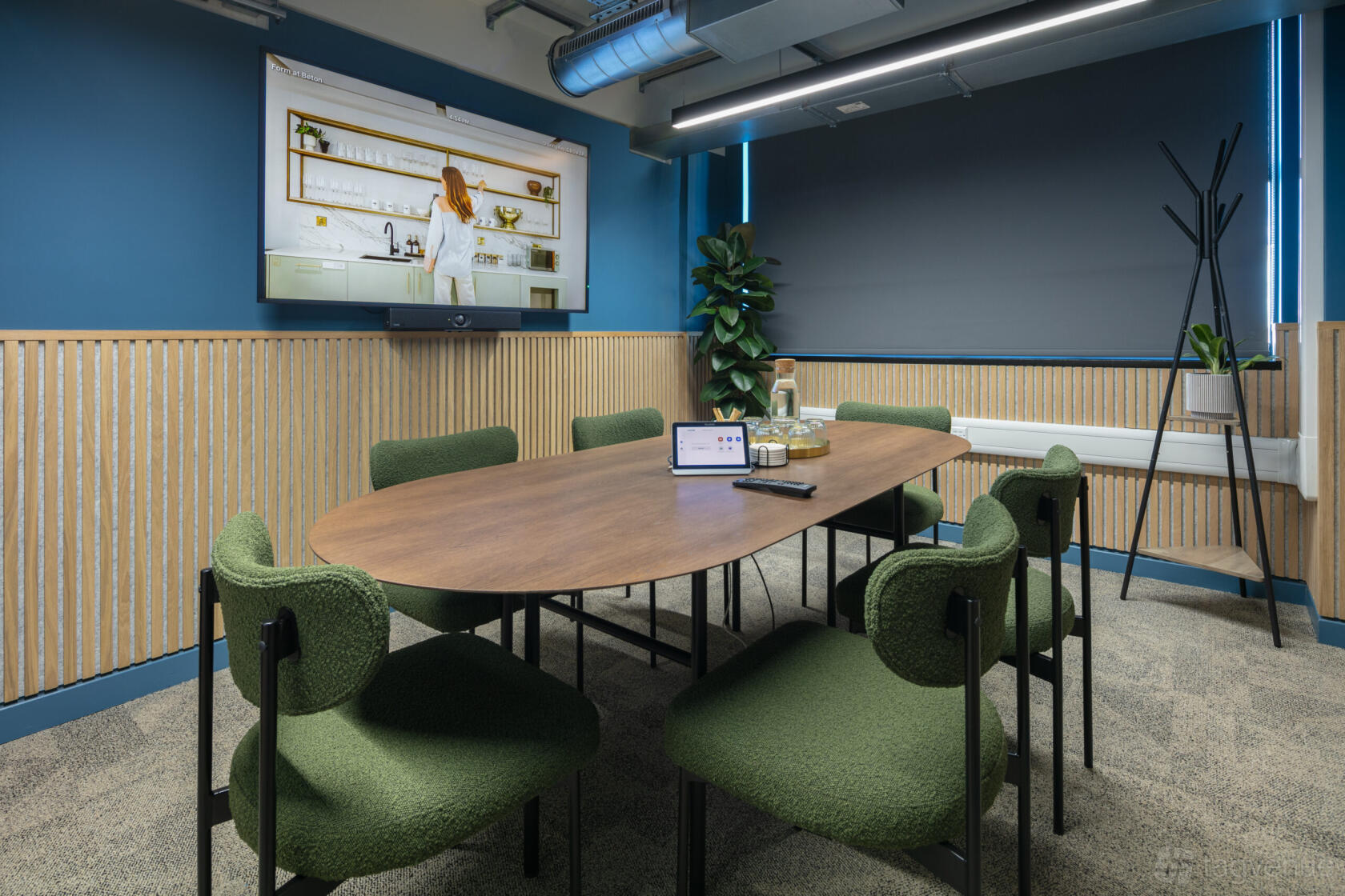A meeting room with a large oval table, green upholstered chairs, wall-mounted screen, and potted plant at Spacemade - Beton.