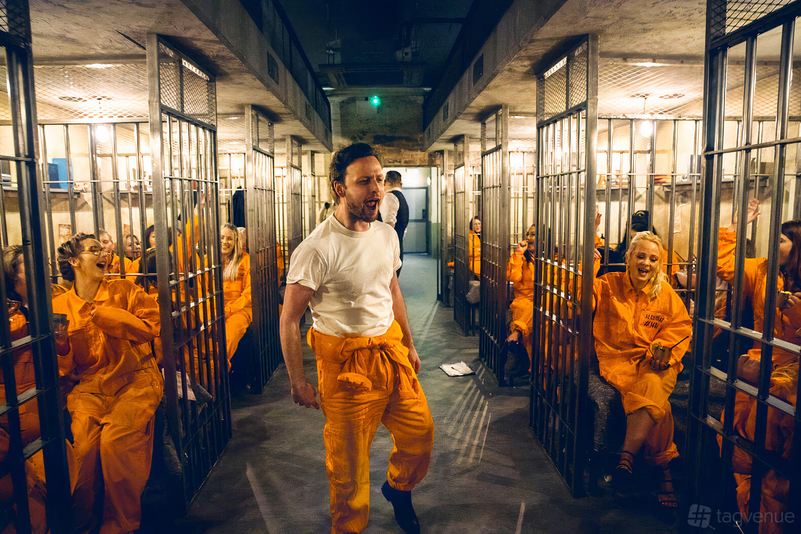 A cocktail bar with metal prison cell decor and guests in orange jumpsuits at Alcotraz Manchester.