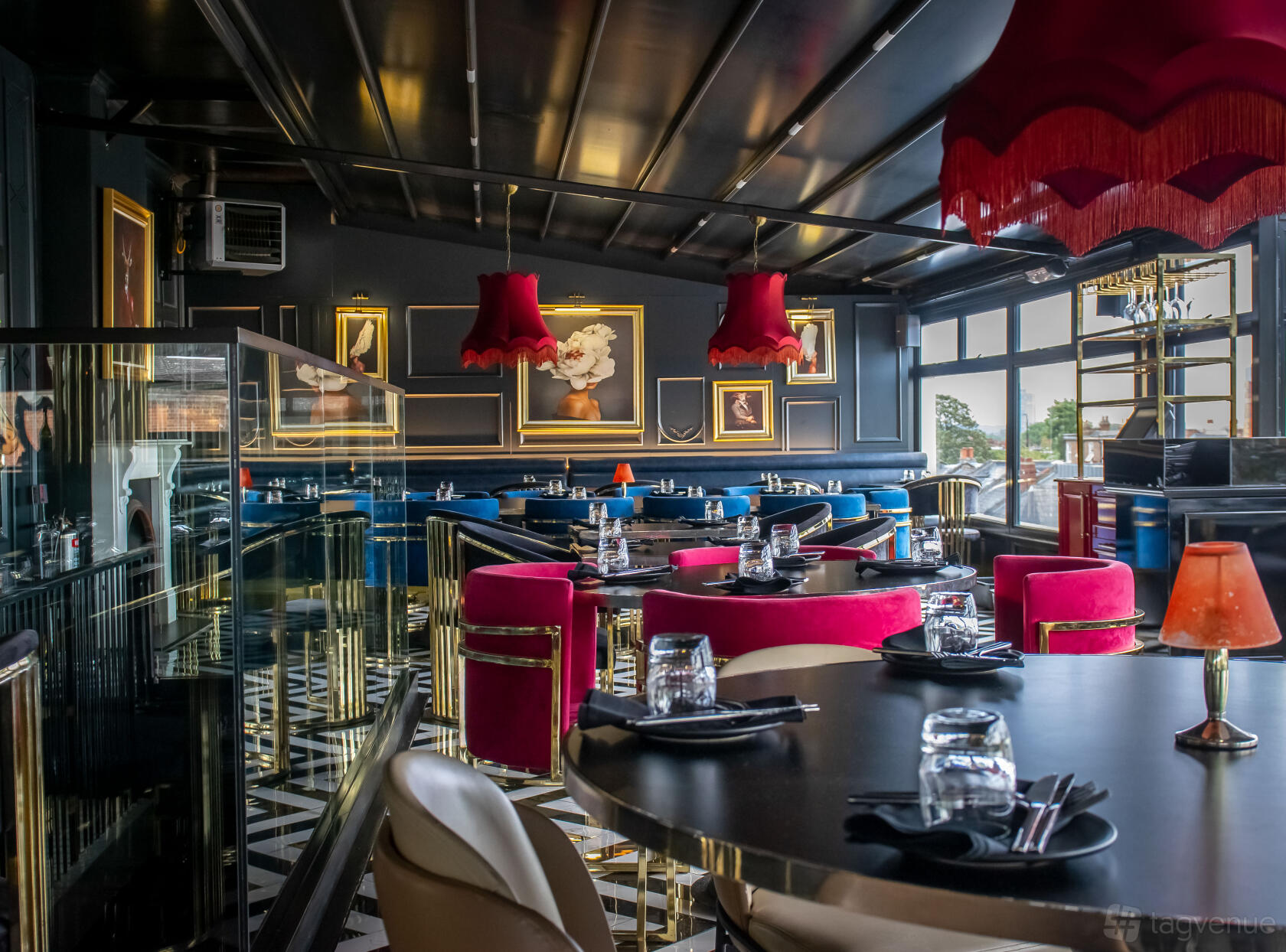 A rooftop restaurant with patterned floors, velvet seating, red pendant lamps, and framed artwork at Tarshish.