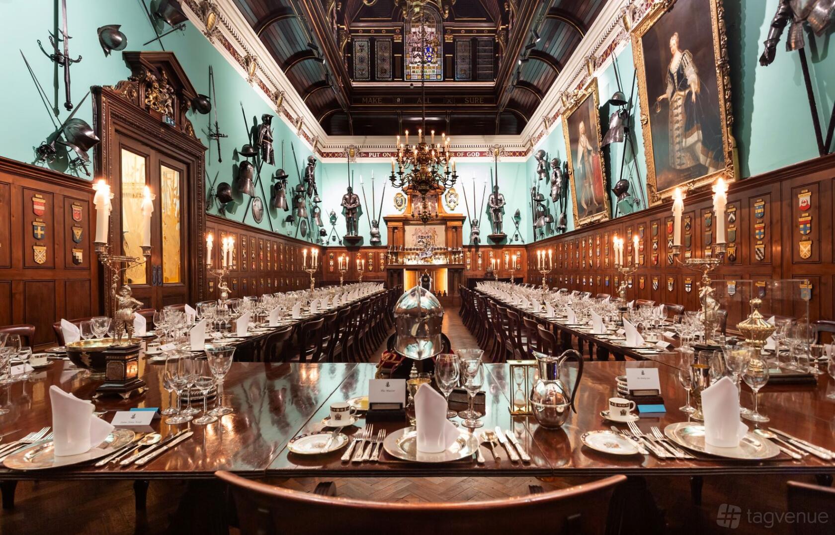 A grand hall with high ceilings, stained glass windows, suits of armor, and long banquet tables at Armourers' Hall.