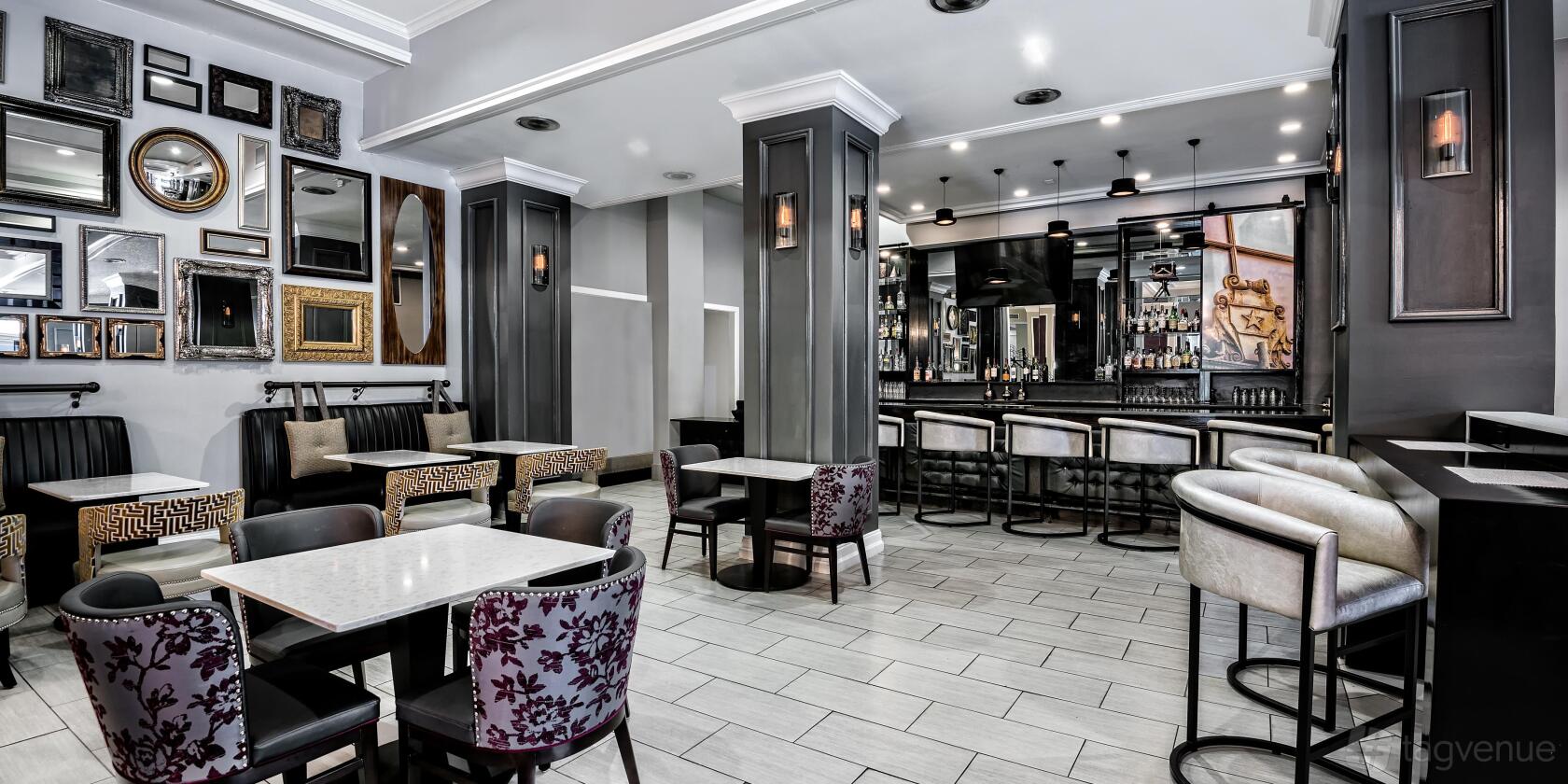 A hotel bistro and bar with patterned chairs, framed wall art, and a marble-topped bar at Hotel Indigo Dallas Downtown.