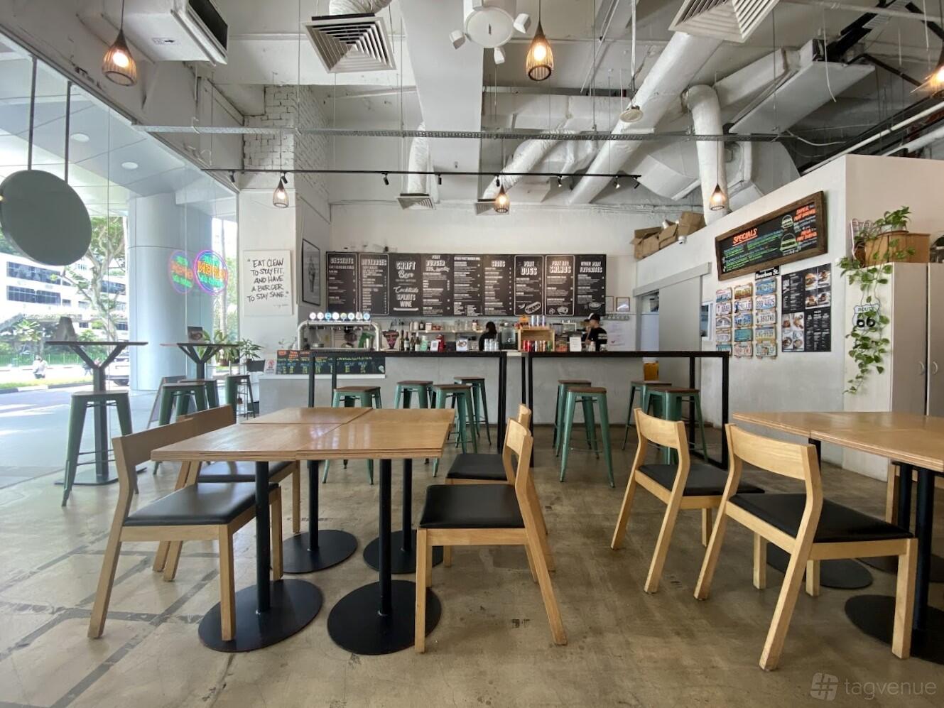 A restaurant with wooden tables, black chairs, high stools at the counter, and large windows at Phat Burger Bro.