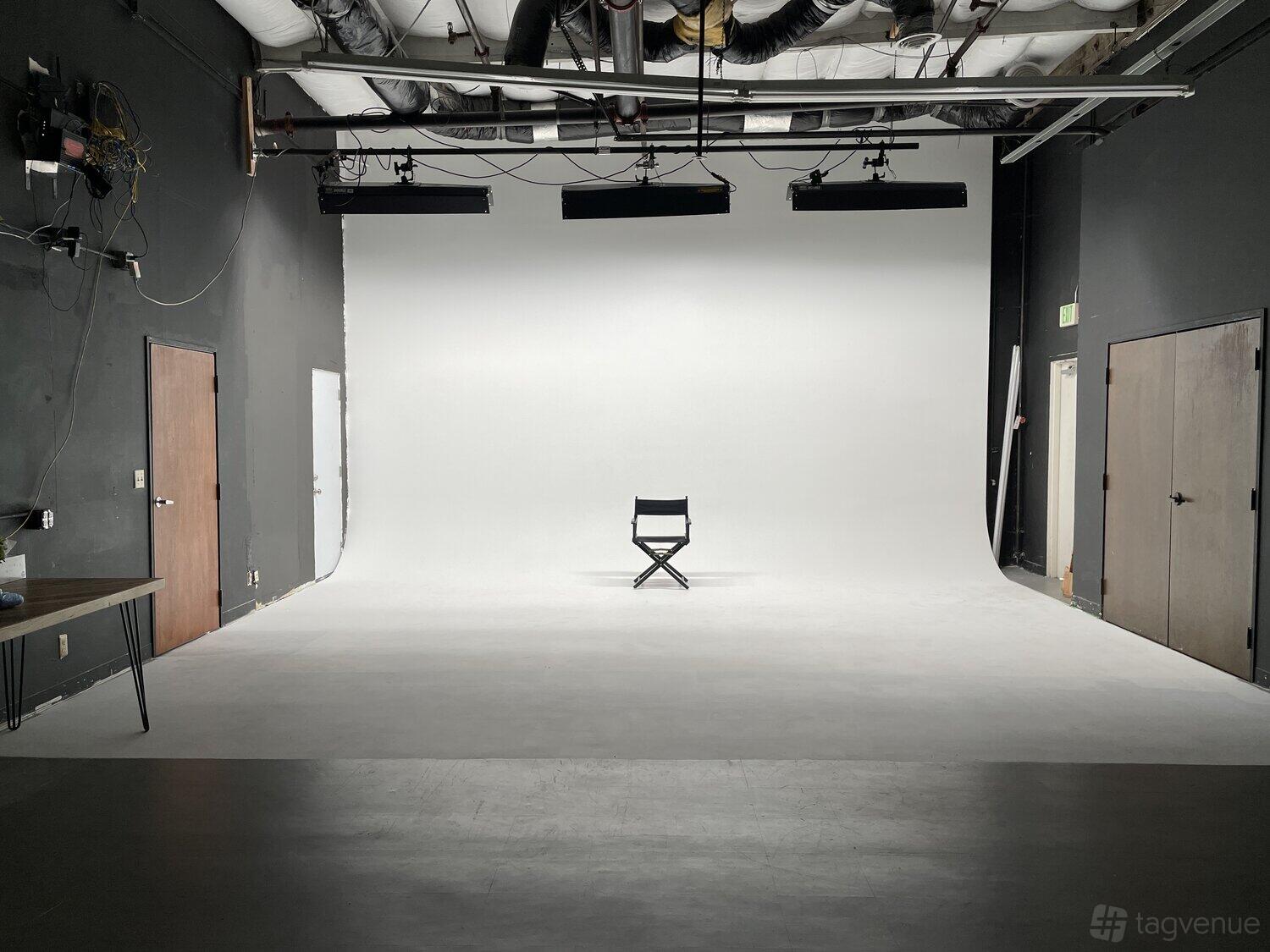 A meeting centre with a white cyclorama wall, overhead lighting rigs, and a single director’s chair at StageOne Creative Stages @ Milpitas.