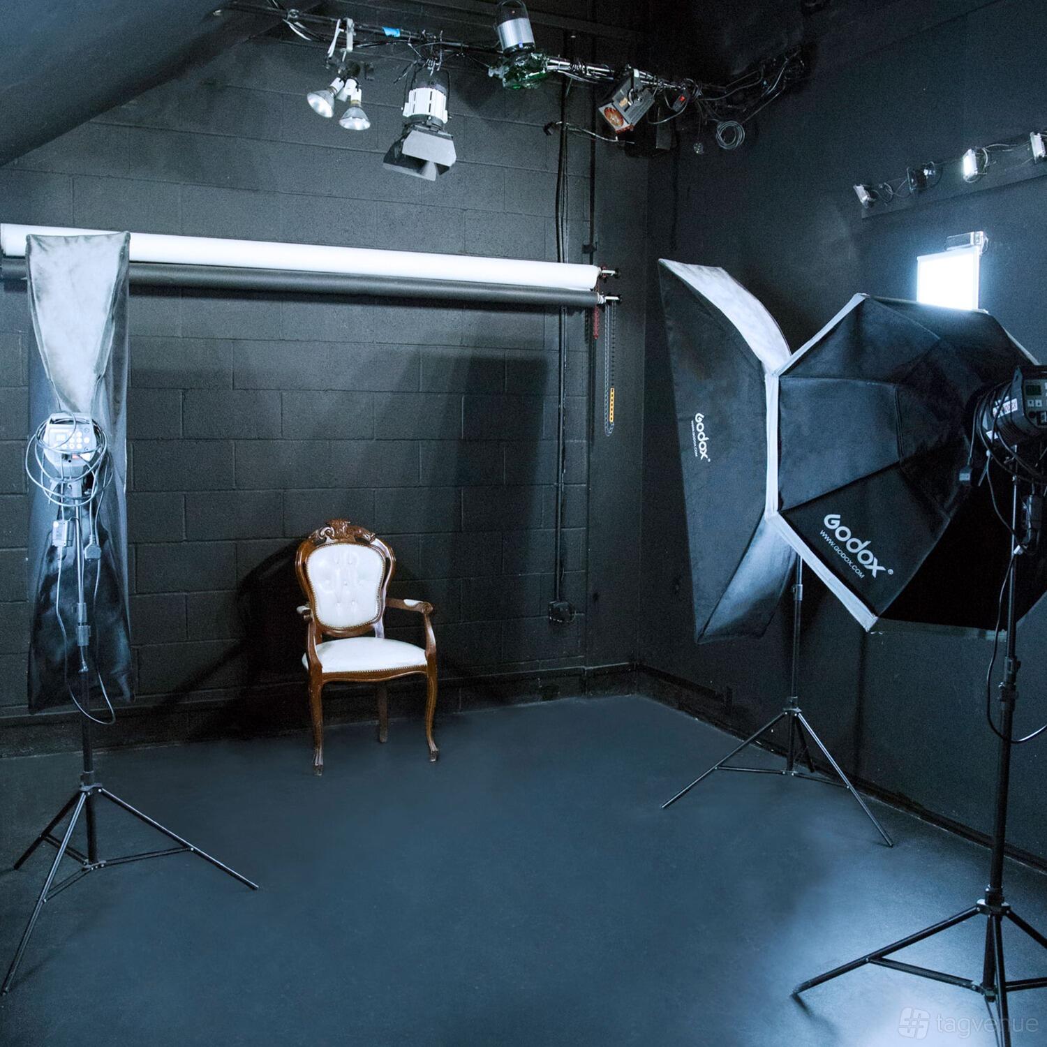A photo studio with black walls, a vintage chair, white backdrop, and large softbox lighting at AFFilms Studio 101.
