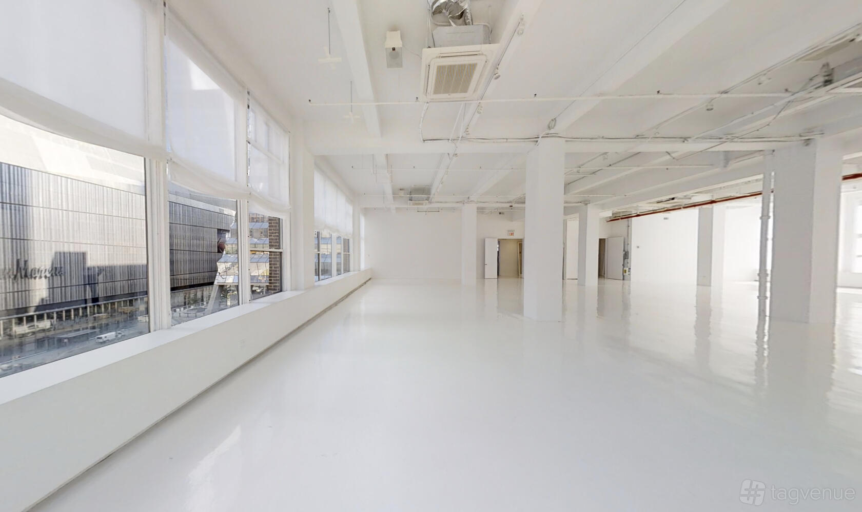 An event venue with floor-to-ceiling windows, polished white floors, and exposed ceiling pipes at Location 05.