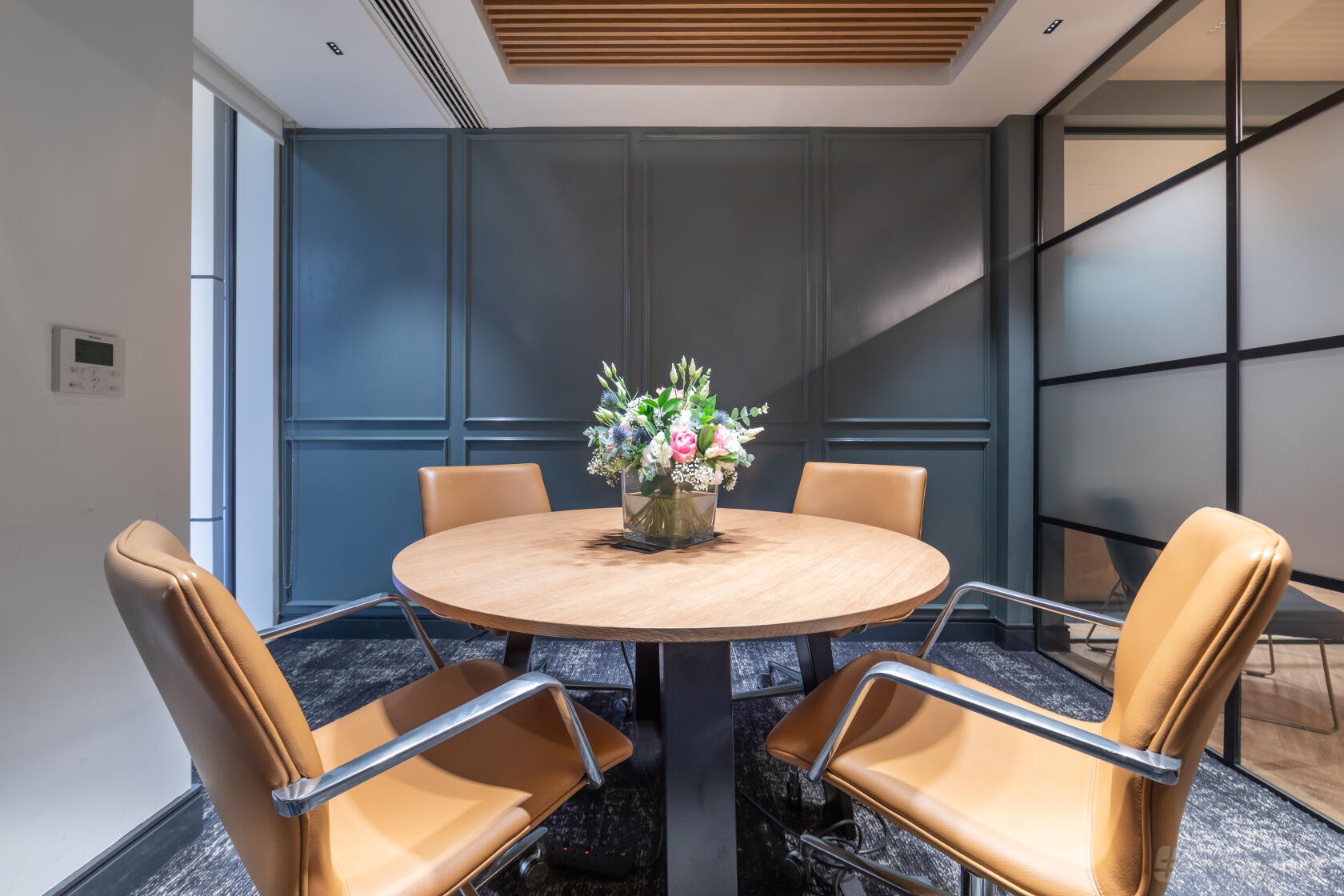 A meeting centre with a round wooden table, four tan leather chairs, and a flower arrangement at Landmark: Chancery Lane, London.