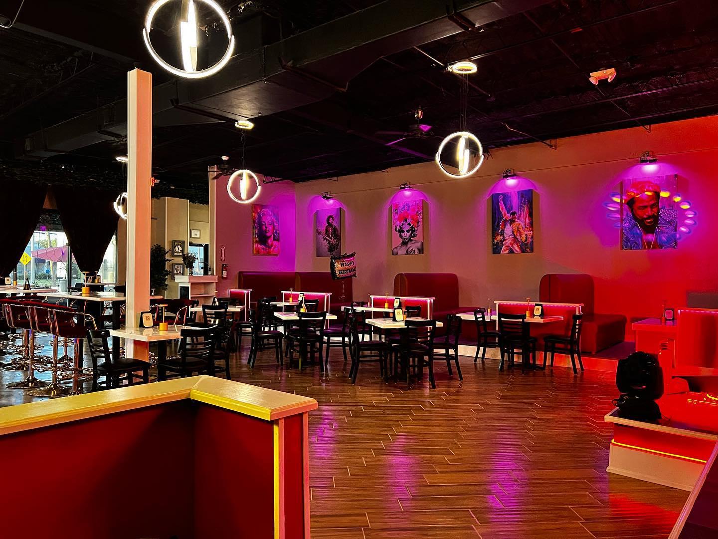A bar with red booths, round tables, wood flooring, neon lighting, and music-themed wall art at Monarch Bar and Lounge.