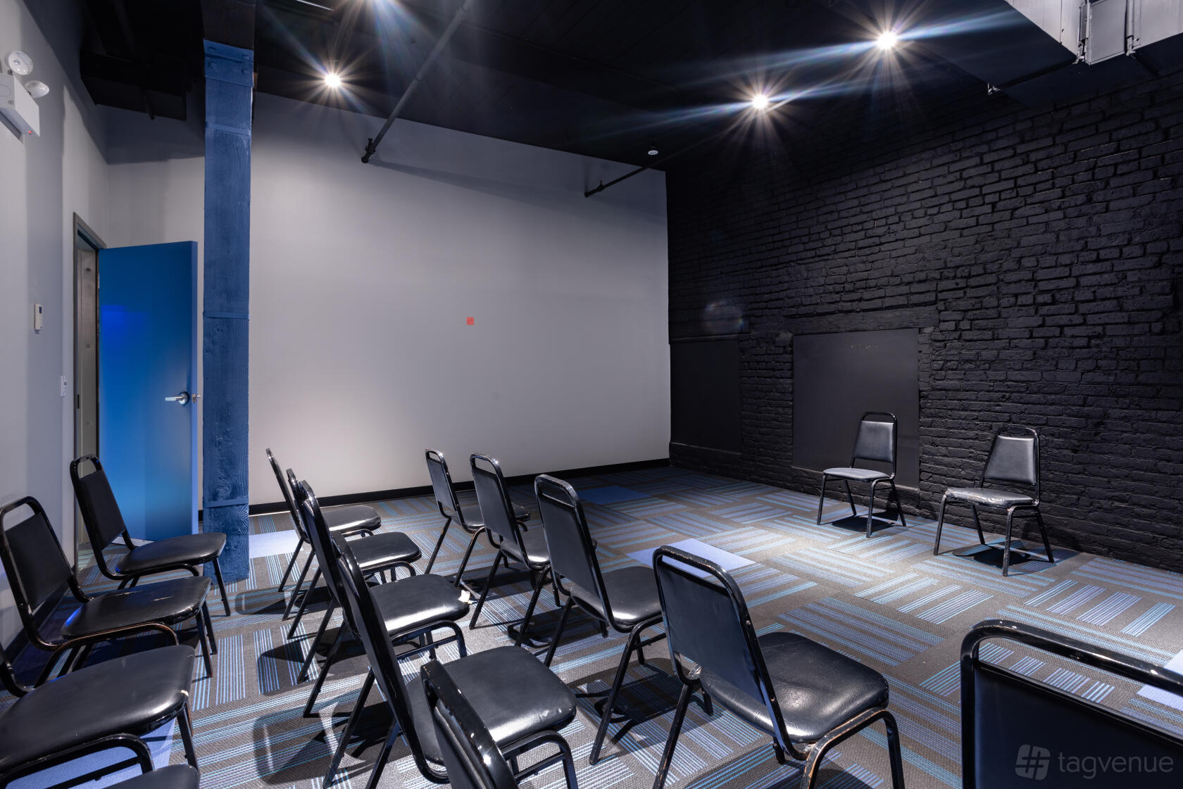 A classroom in a theatre with black brick walls, blue carpet, and rows of black chairs at iO Theater.