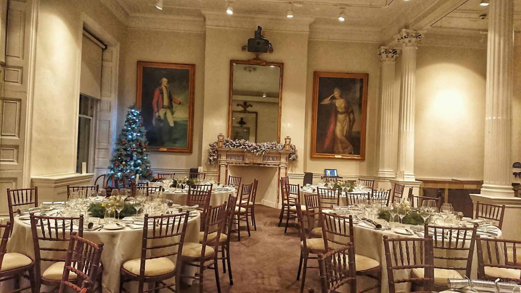 An event venue with round tables set for dining, tall windows, classical columns, and large portraits at 41 Portland Place.