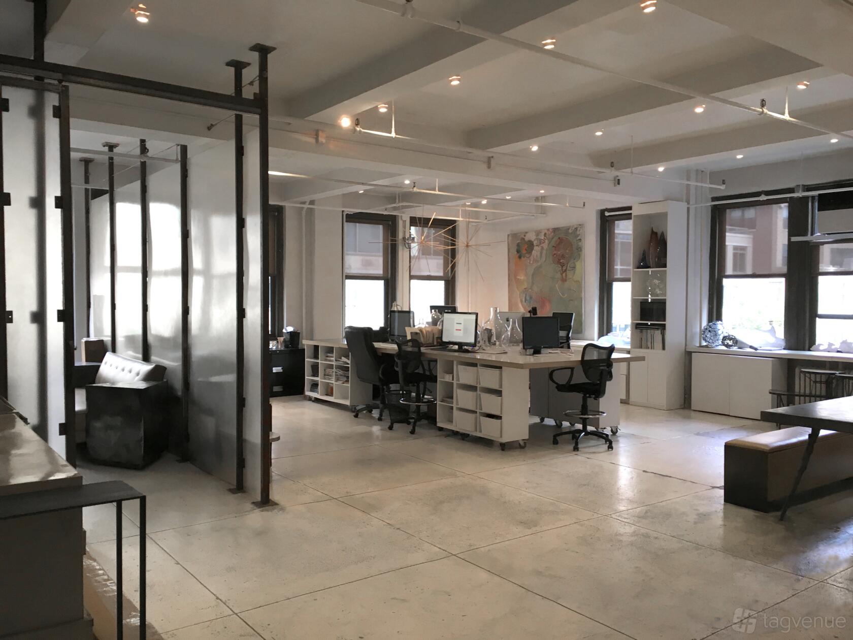 An open event space with large windows, exposed beams, frosted glass dividers, and desks at Office Space Midtown-Manhattan.