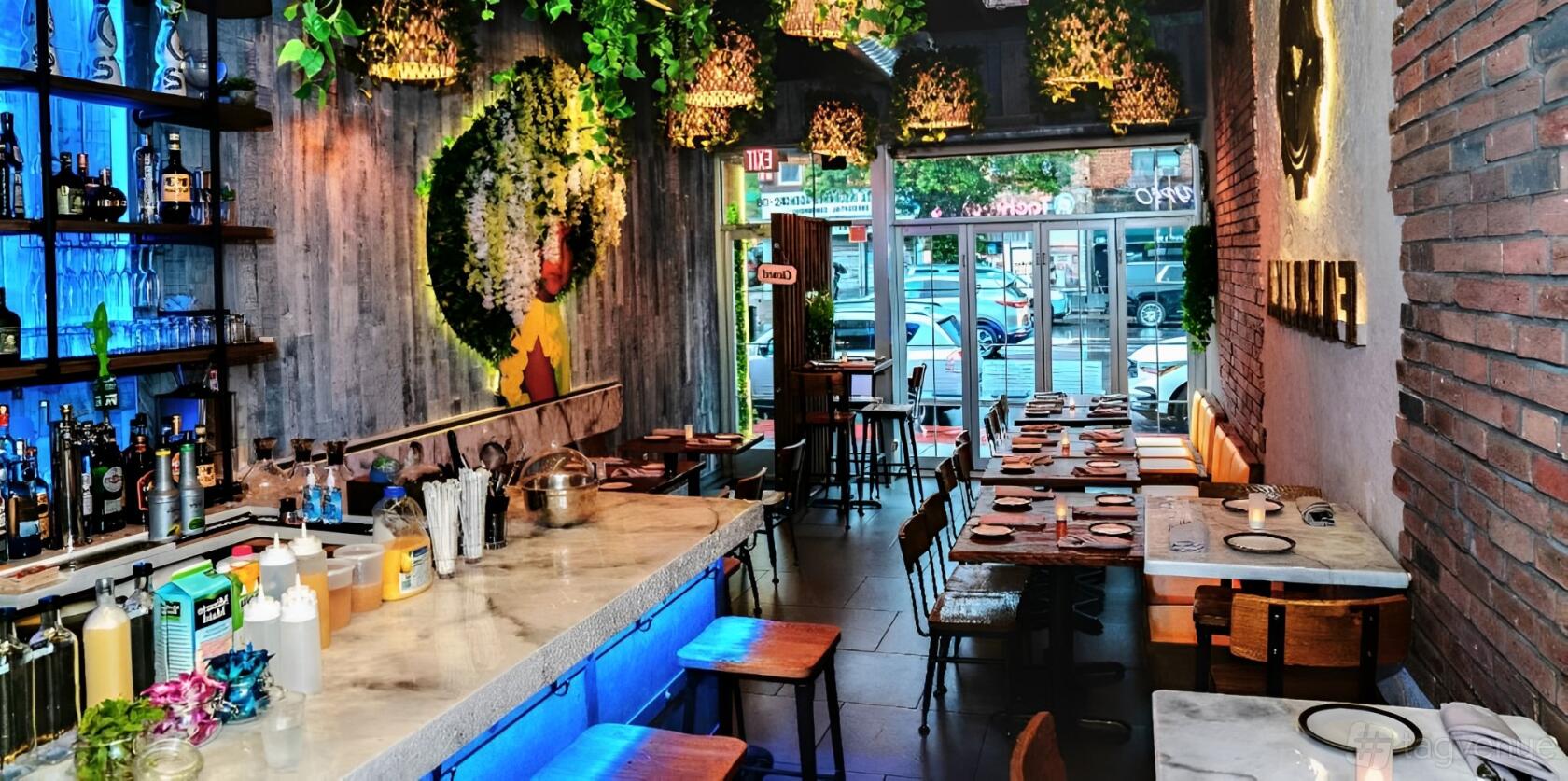 A restaurant with a marble-topped bar, hanging greenery, wooden tables, and floor-to-ceiling windows at Fabrika.