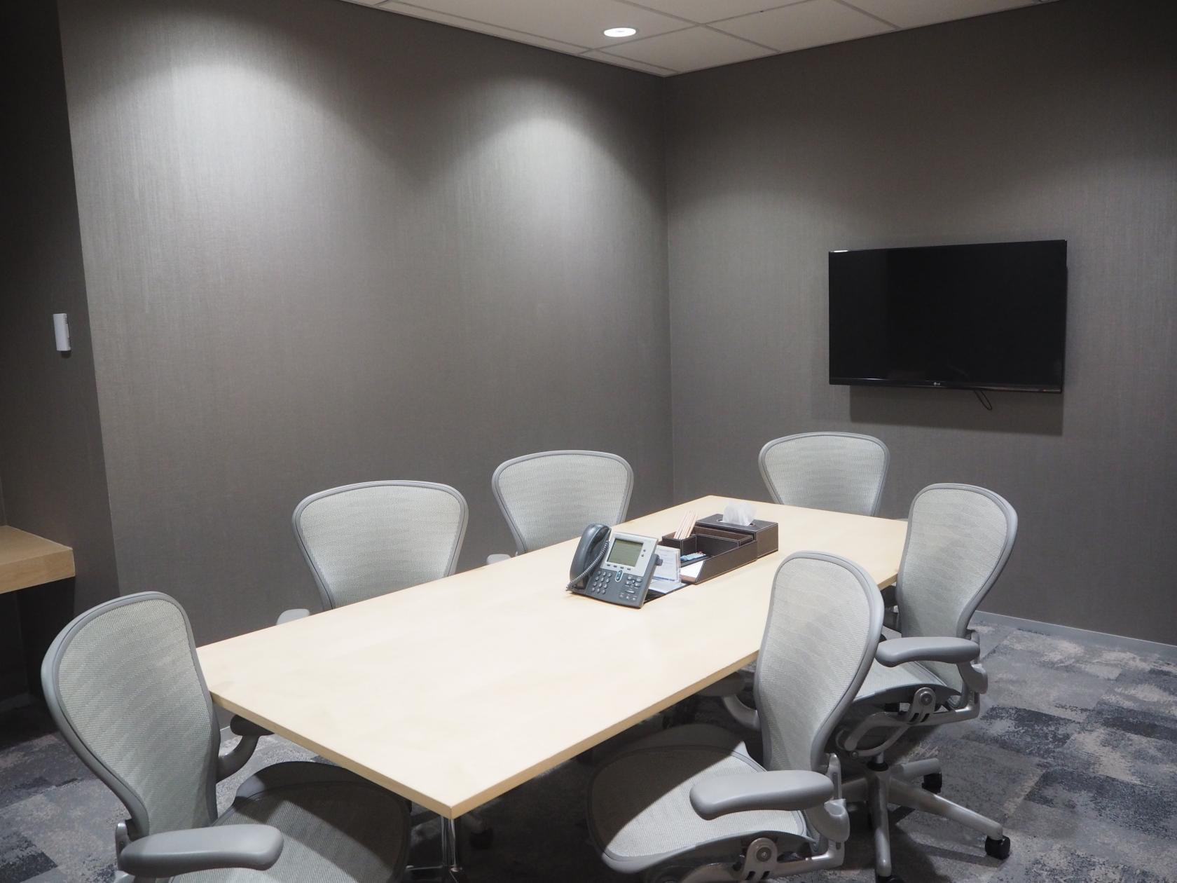 A meeting room with a rectangular table, six ergonomic chairs, wall-mounted TV, and conference phone at 108 St Georges Terrace.