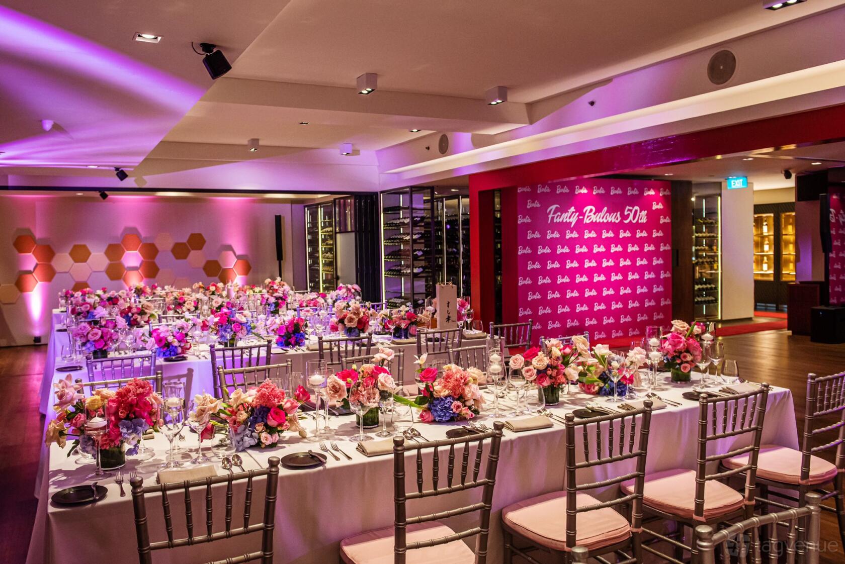 A restaurant dining room with long banquet tables, pink and gold decor, and floral centerpieces at Alma by Juan Amador.