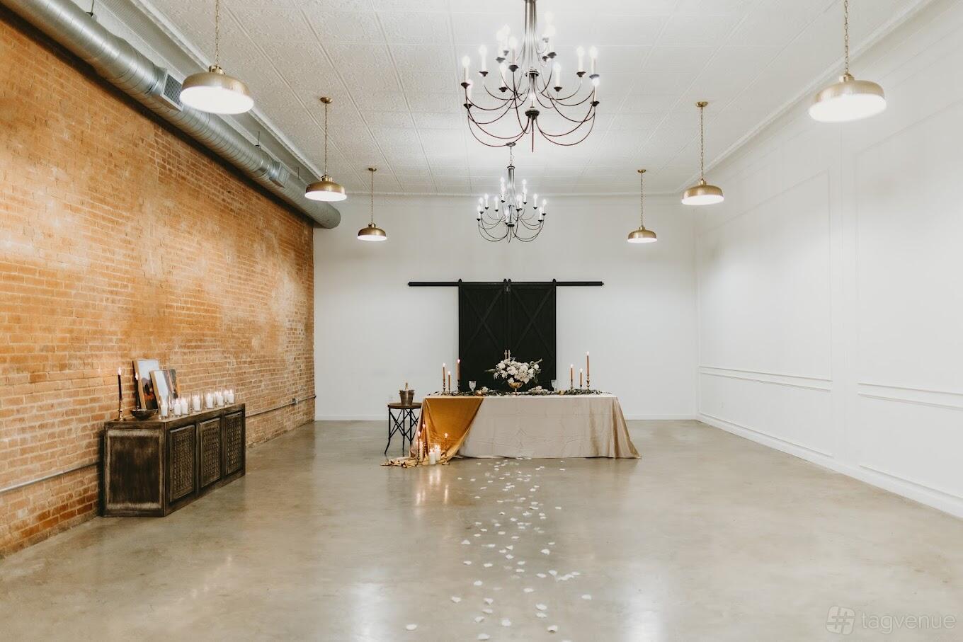A function room with exposed brick walls, chandeliers, and a long table with candles at Space on West Main.