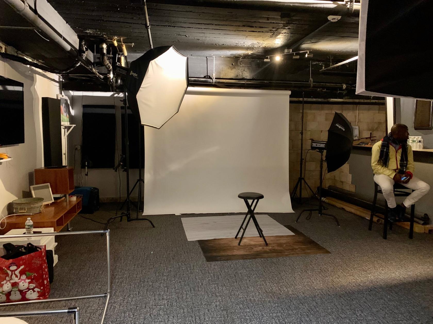 A photo studio with seamless white backdrop, softbox lighting, and a central stool at Green Leaf Multimedia Studio.