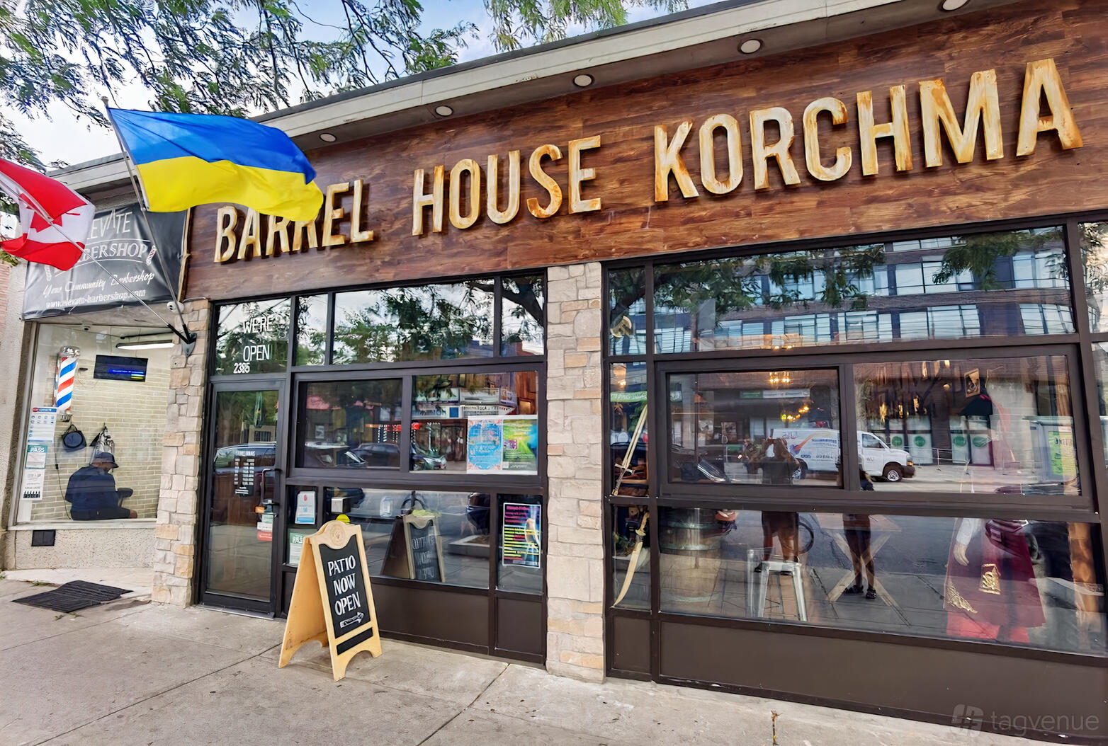 A restaurant exterior with large glass windows, wood signage, and a sandwich board at Barrel House Korchma.