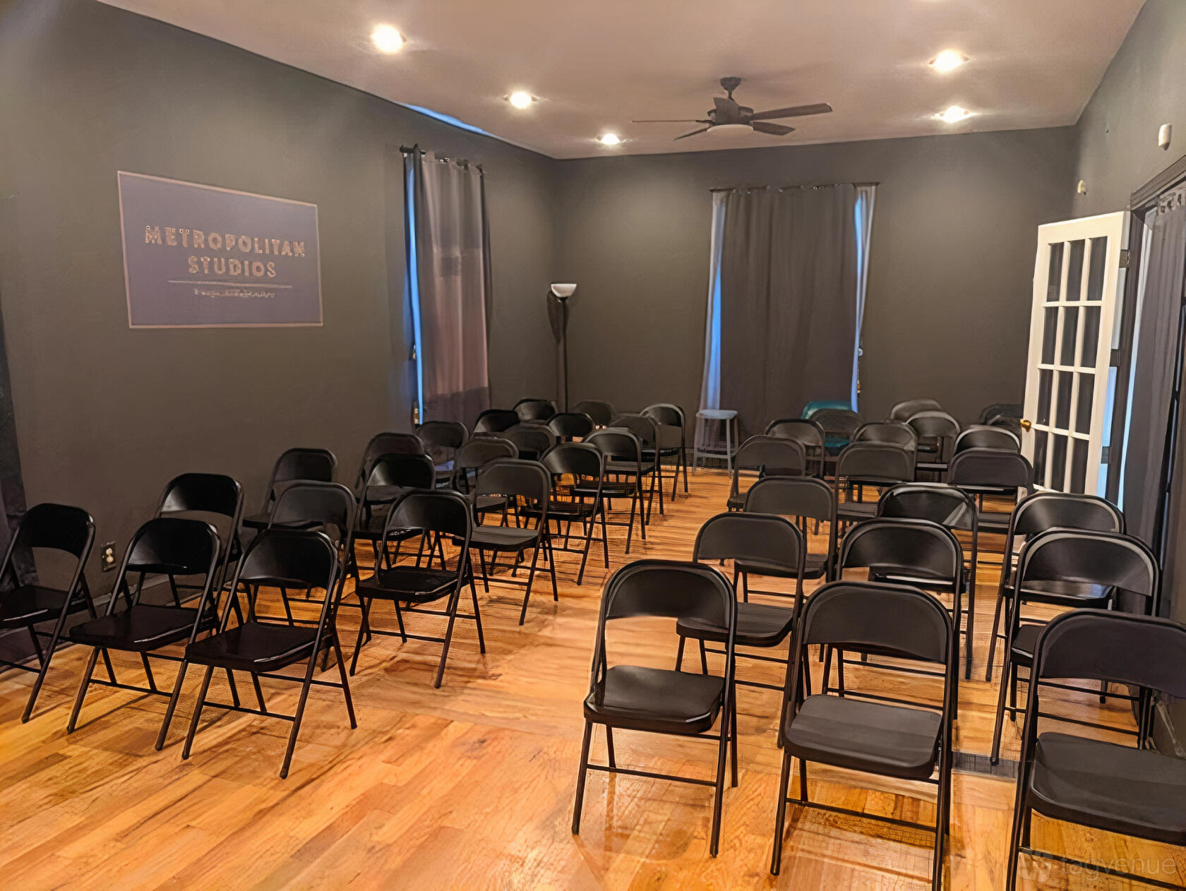 A dance studio with rows of black folding chairs on hardwood floors and dark walls at Metropolitan Studios.