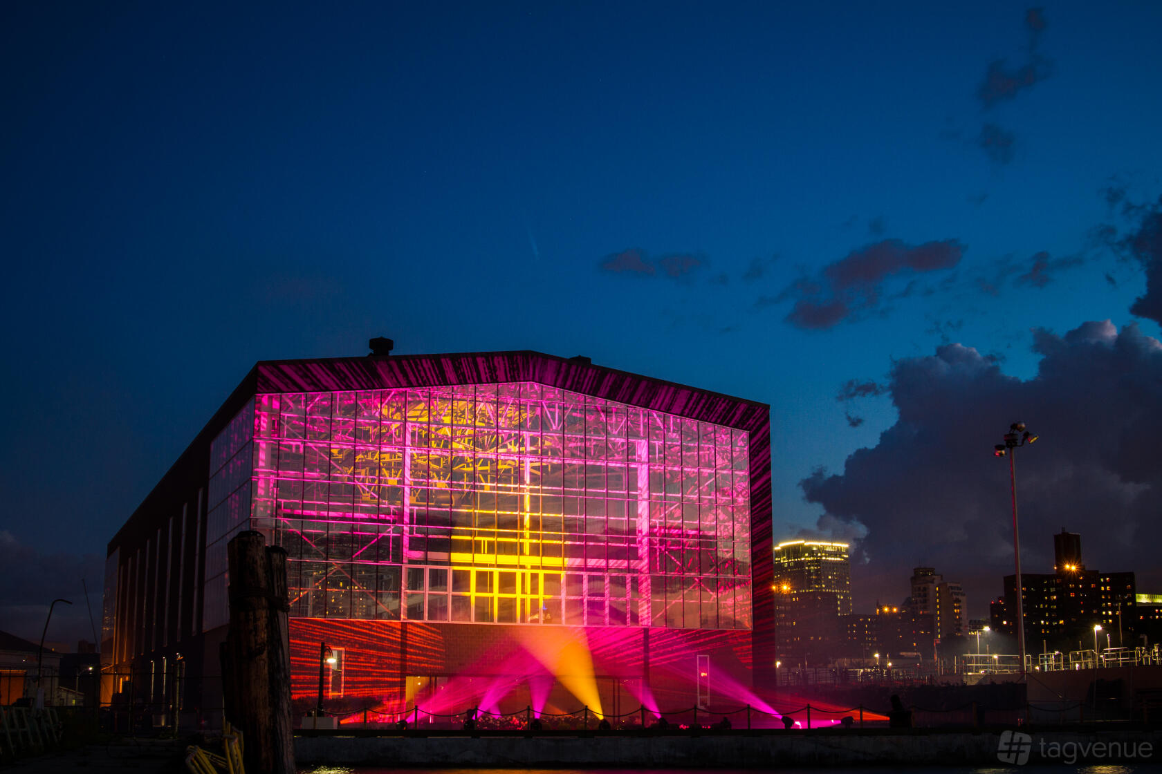 A warehouse with illuminated glass facade and colorful uplighting against the evening skyline at Duggal Greenhouse.