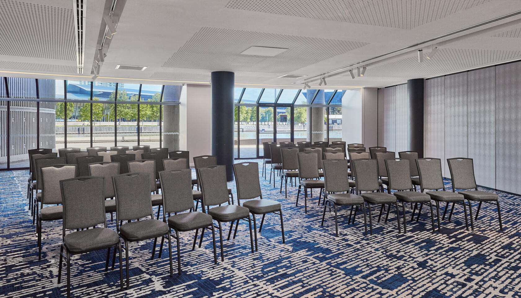 A meeting room with rows of black chairs, patterned carpet, and large river-facing windows at Pearl Riverfront.