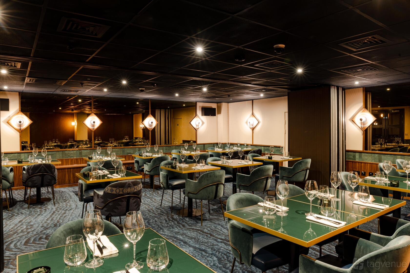 A restaurant dining room with green velvet chairs, glass-topped tables, and geometric wall sconces at Gaucho City.