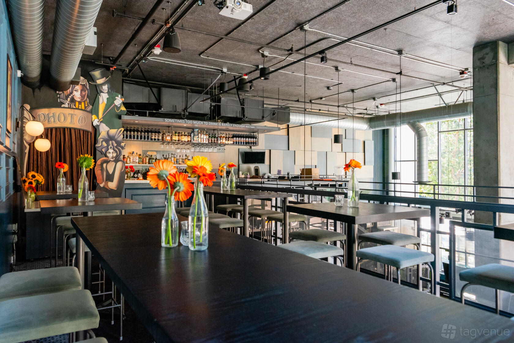An event space with high-top tables, vase centerpieces, and a mural by the bar at Prank.