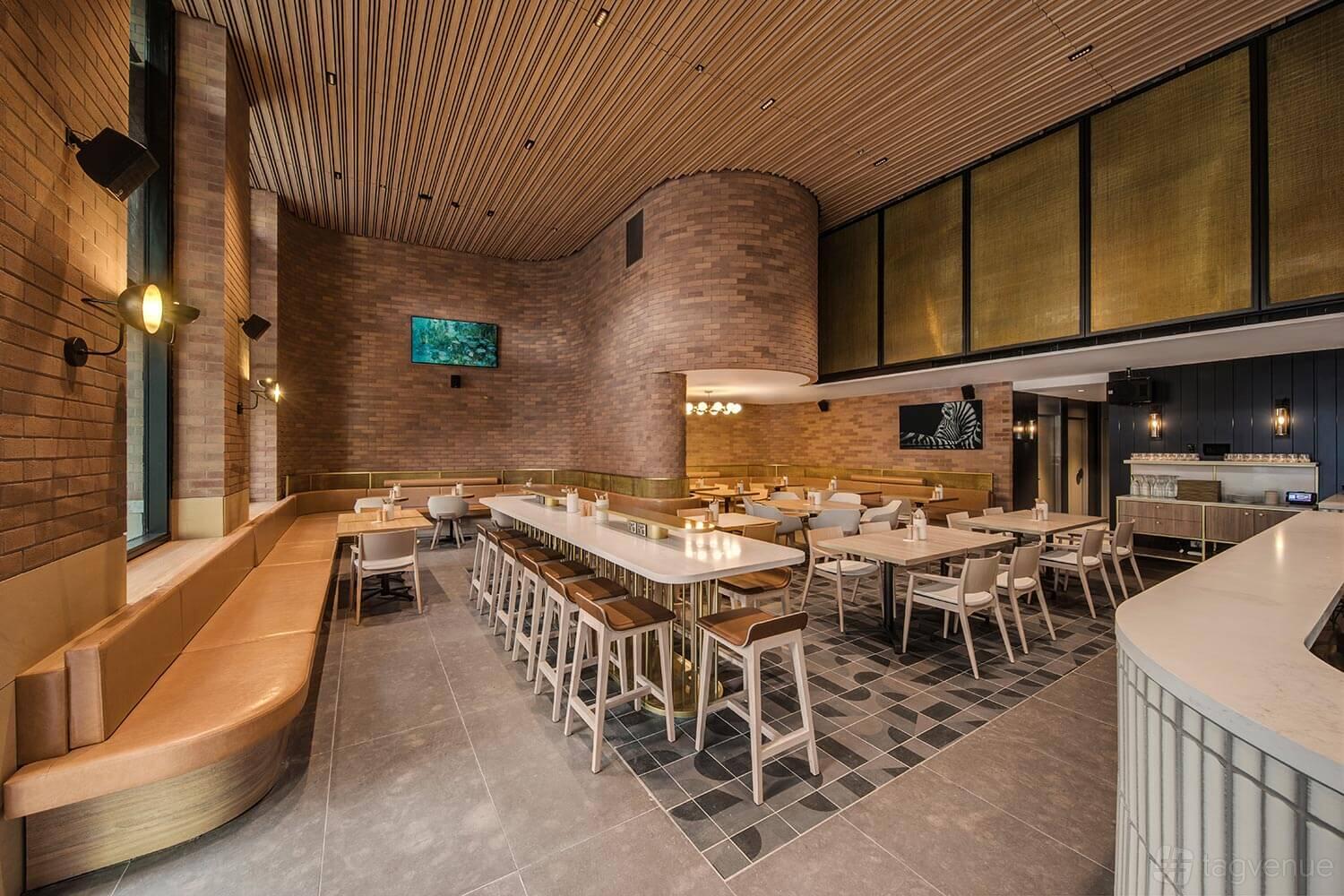 A restaurant with curved brick walls, long communal tables, tan banquette seating, and modern lighting at Vibe Hotel Sydney Darling Harbour.