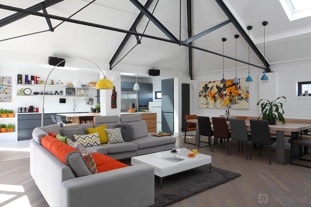 An apartment with exposed steel beams, a large sectional sofa, colorful accents, and an open kitchen at Woolly Mammoth spaces.