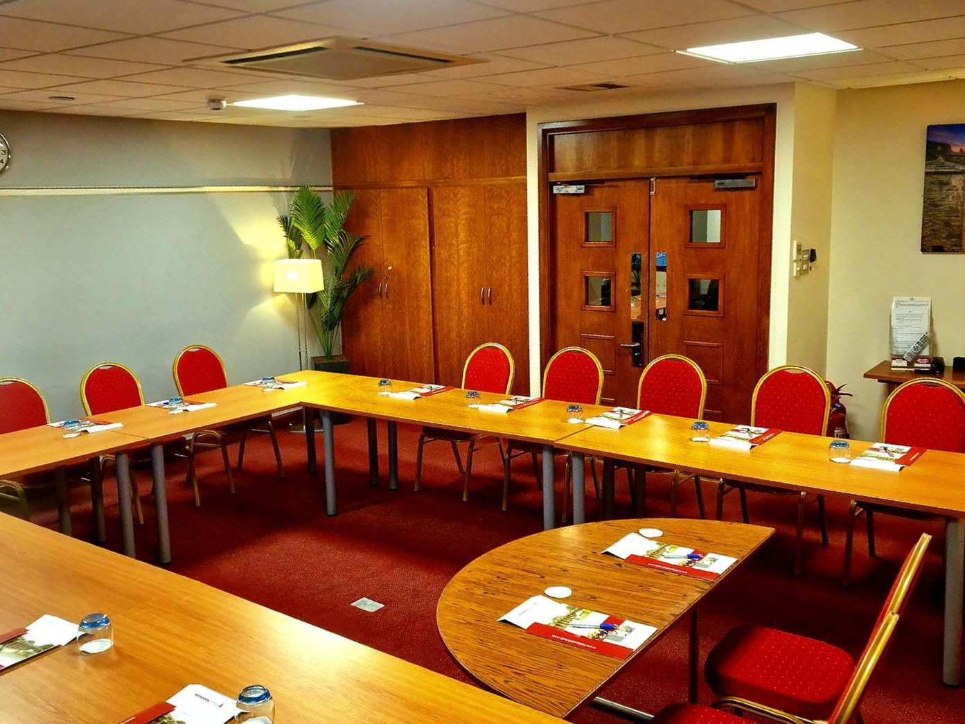 A hotel meeting room with U-shaped tables, red chairs, and notepads on a red carpet at Britannia Leeds Bradford Airport Hotel.