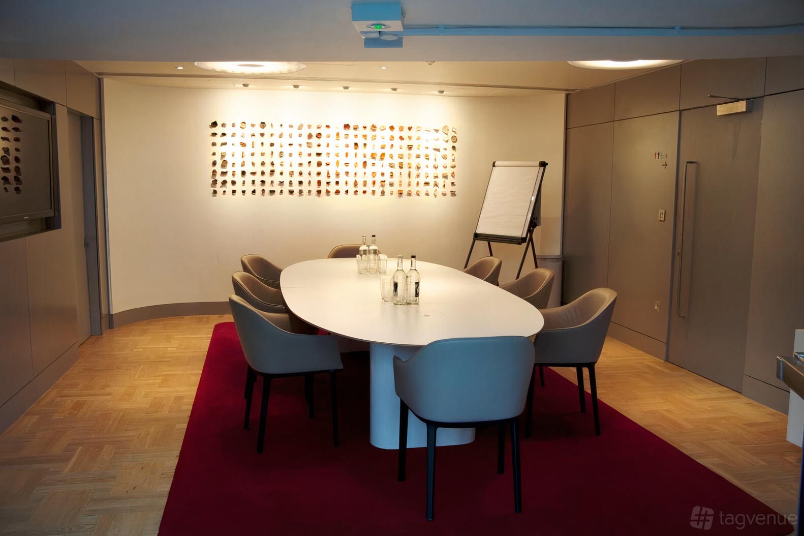 An event space with an oval meeting table, gray chairs, parquet flooring, and art display at London Museum Spaces.